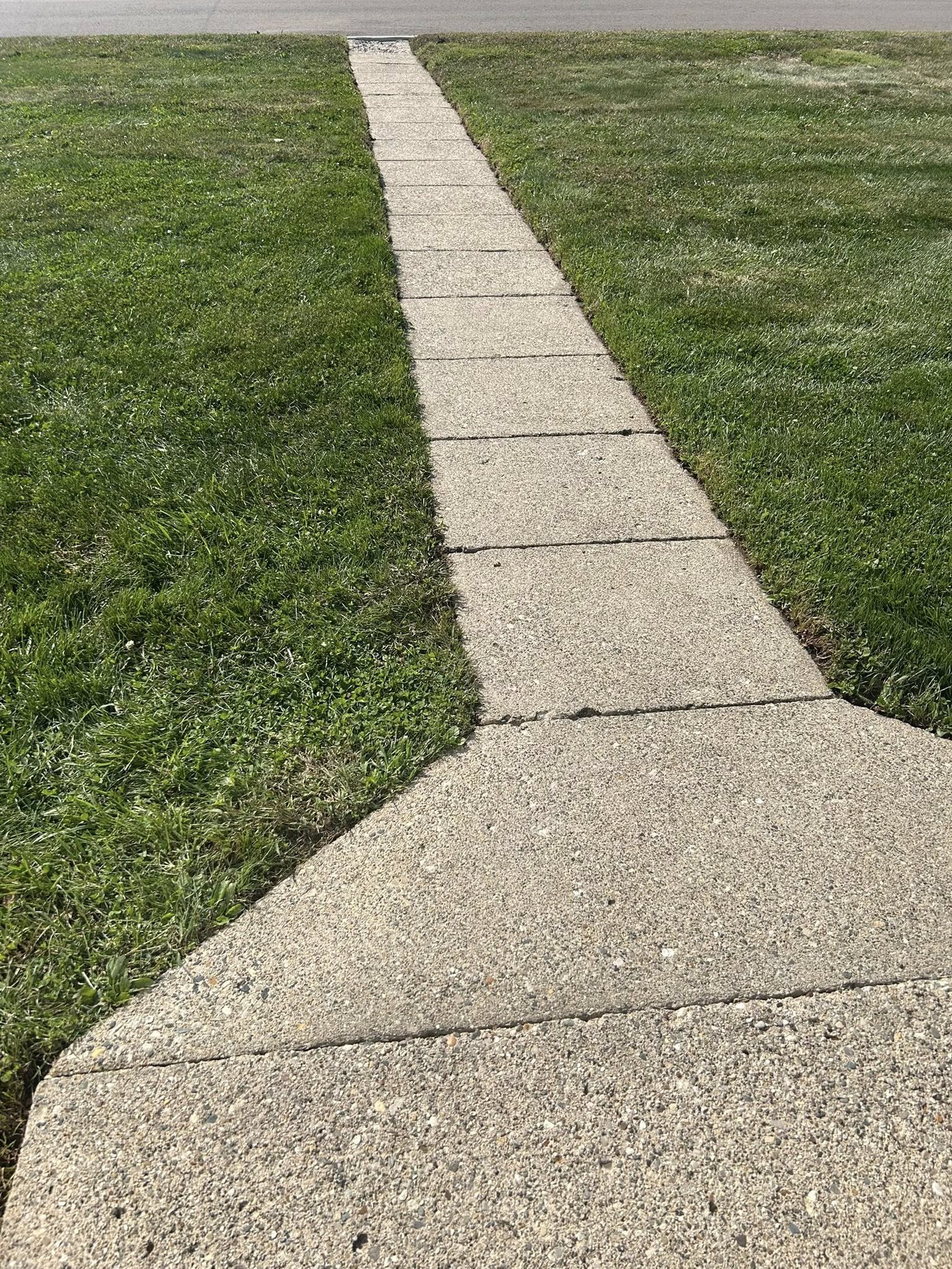 Concrete sidewalk cutting through green lawns on both sides, leading towards the street in the background. After cleaning. 