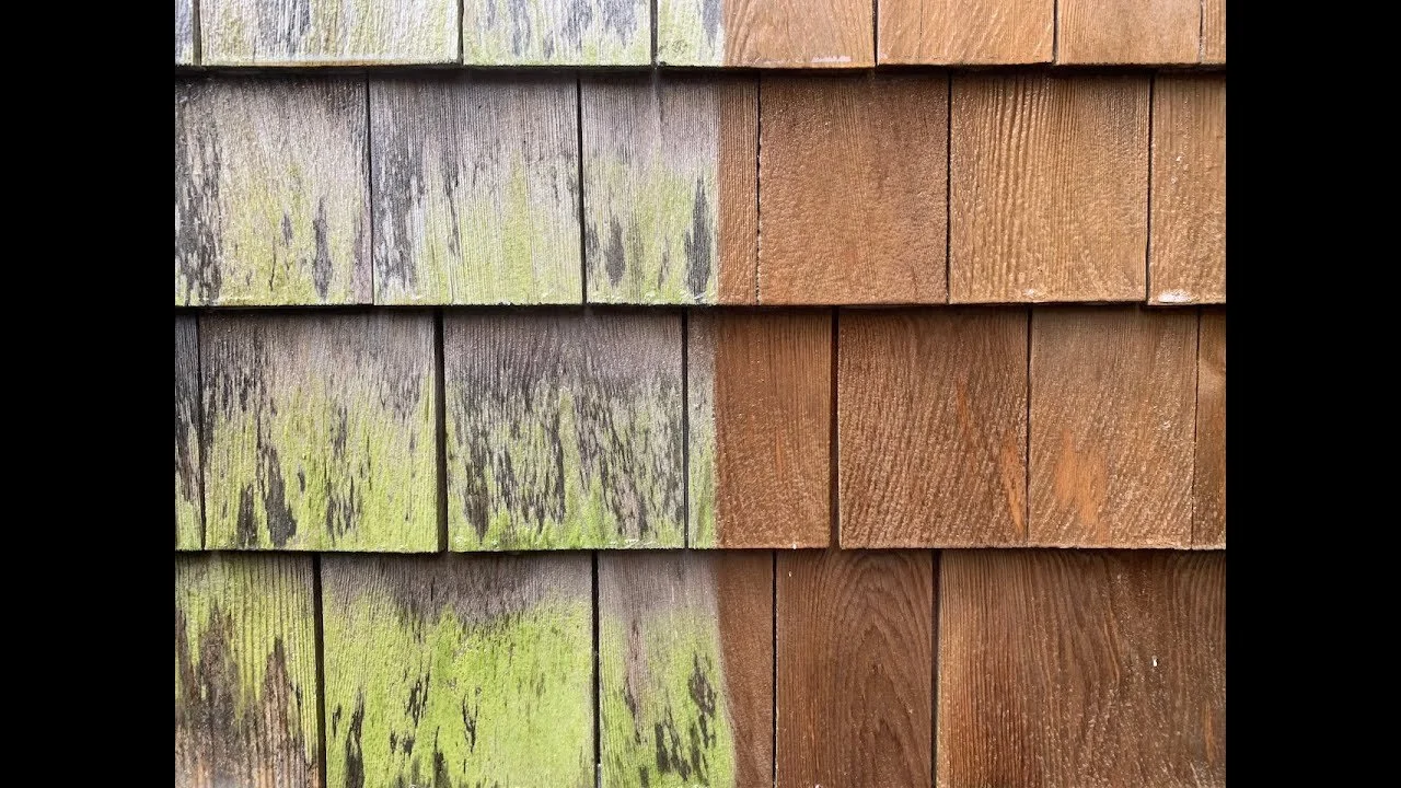 Close-up view of the side of a building with wooden shingles, some of which are weathered with greenish moss and others are newer and brown.