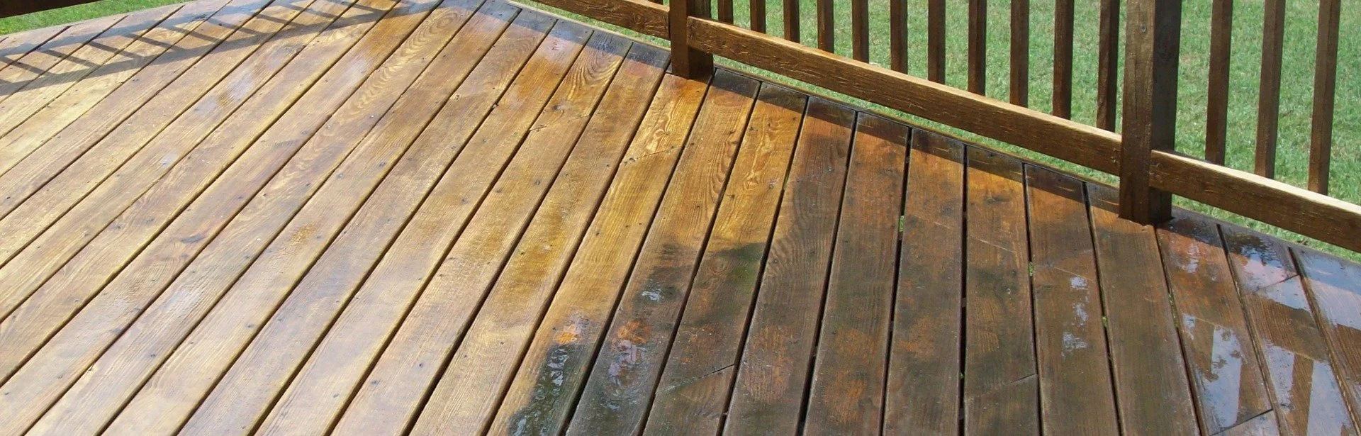 Wet wooden deck with a railing, surrounded by green grass.