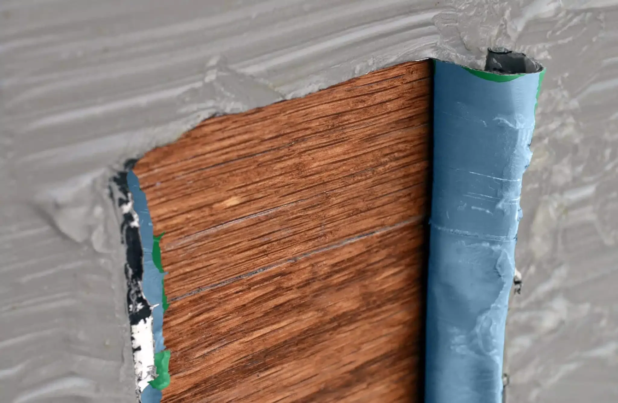 Close-up of damaged wall showing a section of wood paneling with blue and green tape around the edges, and some drywall peeling away.