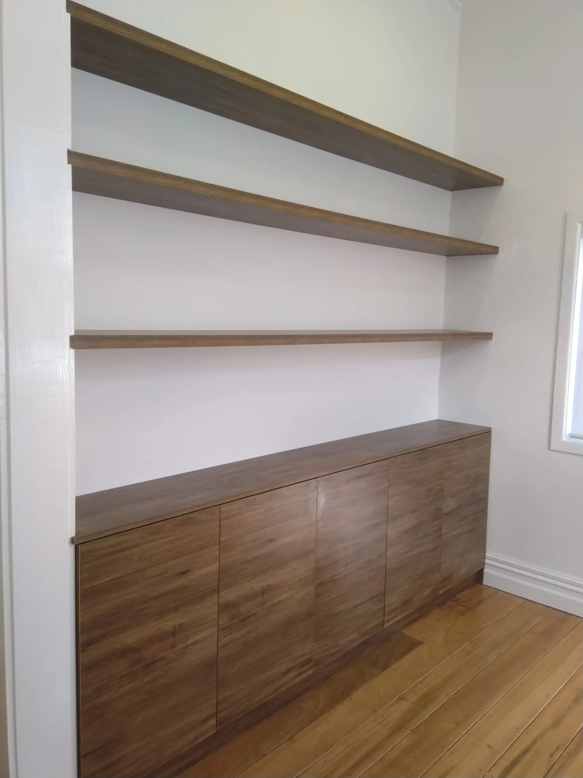 Built-in wooden shelves and cabinet in a room with hardwood floors and a window.