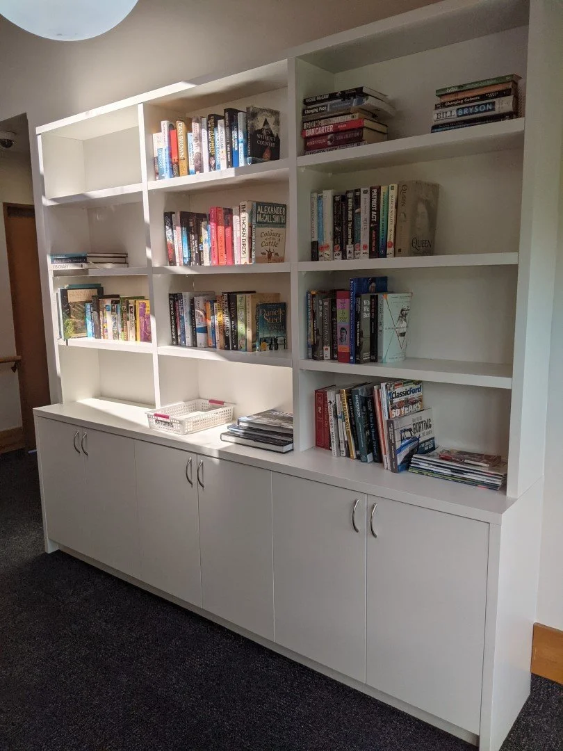 White bookshelf filled with books, some stacked horizontally and others vertically, with a closed cabinet base and silver handles.