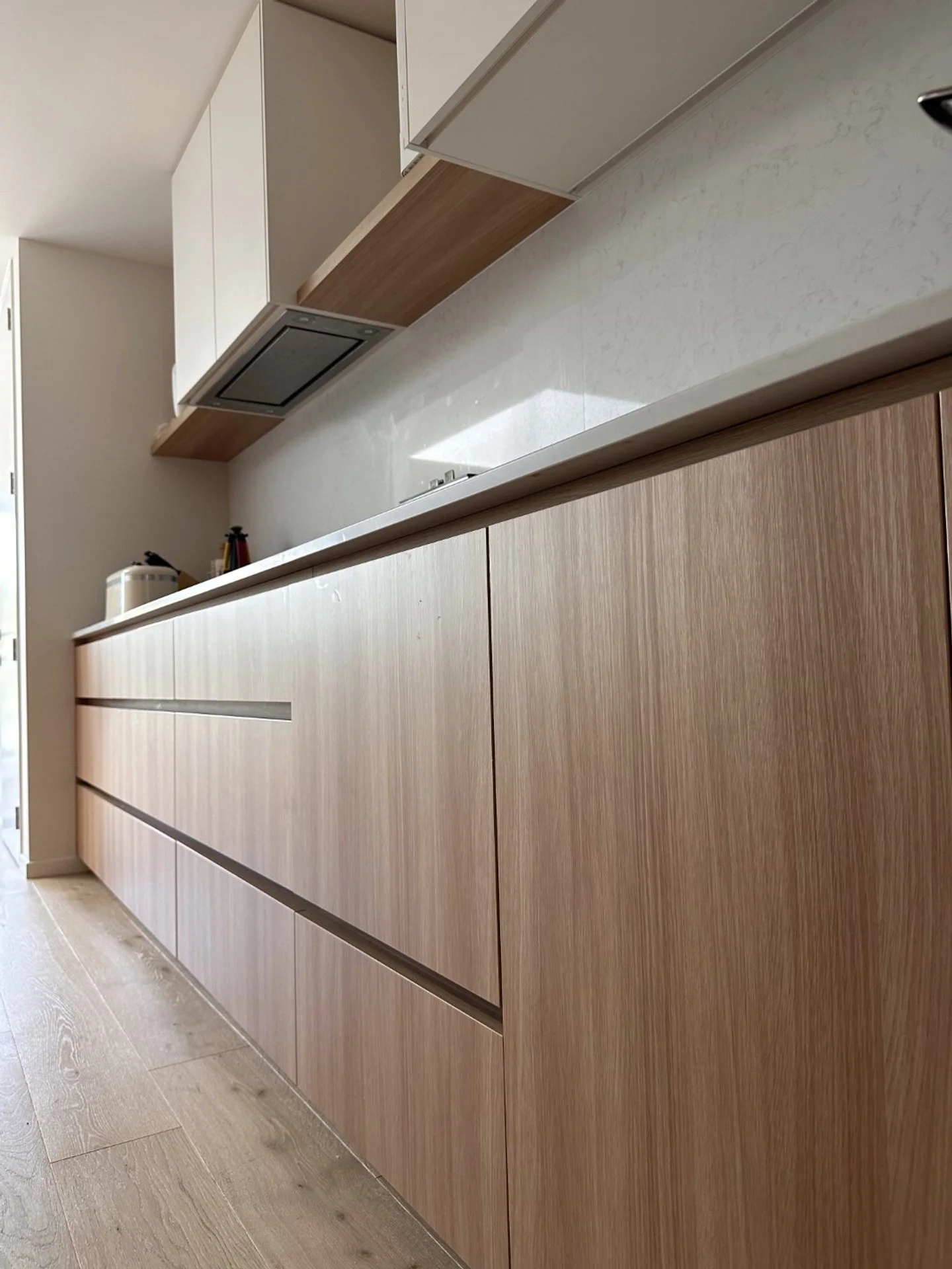 Modern kitchen with light wood cabinets, white countertop, and beige flooring.