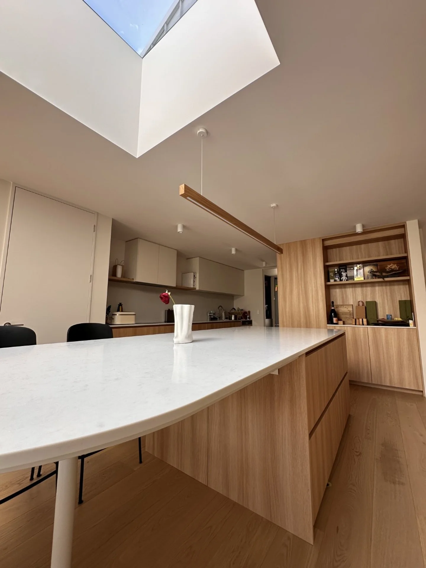 Modern kitchen with a large white marble island, wooden cabinetry, and a skylight ceiling allowing natural light.