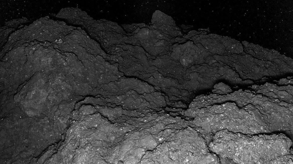 Close-up of dark, rocky terrain with rough, uneven surfaces and small granules.