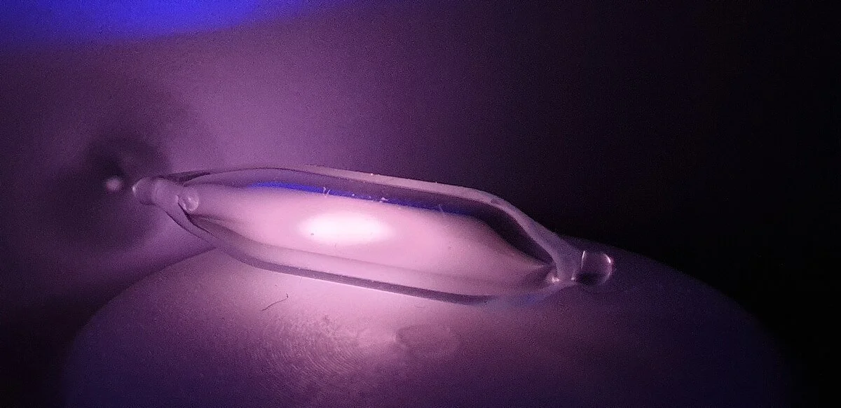A clear ampule with helium-3 gas, illuminated from within, resting on a dark surface.