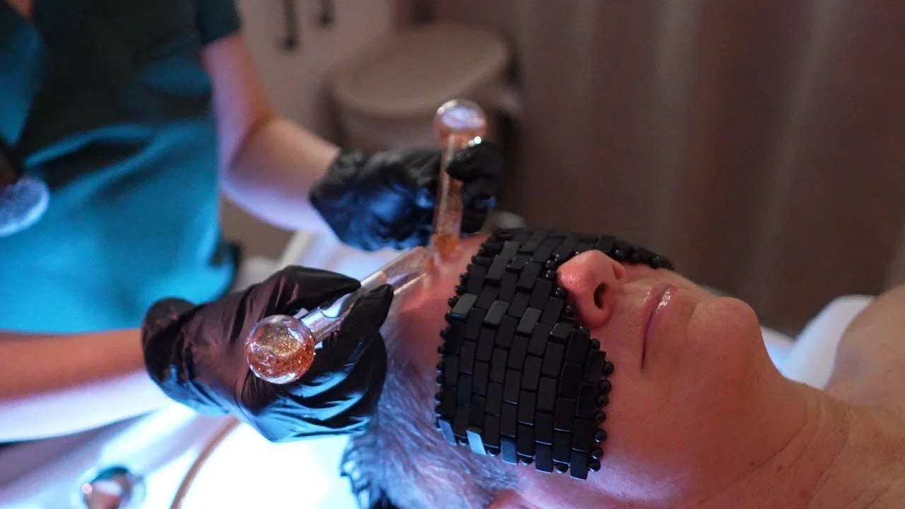 woman getting a massage with two wands on her forehead, and she is laying down with a black eye band over her eyes.