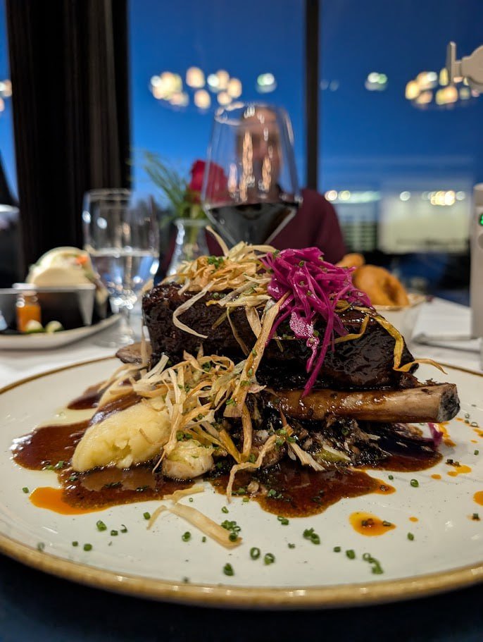 this is a picture of a dish of food, there is beef stacked up on a plate with shredded vegetables that are colourful and a beautiful talbe place setting.