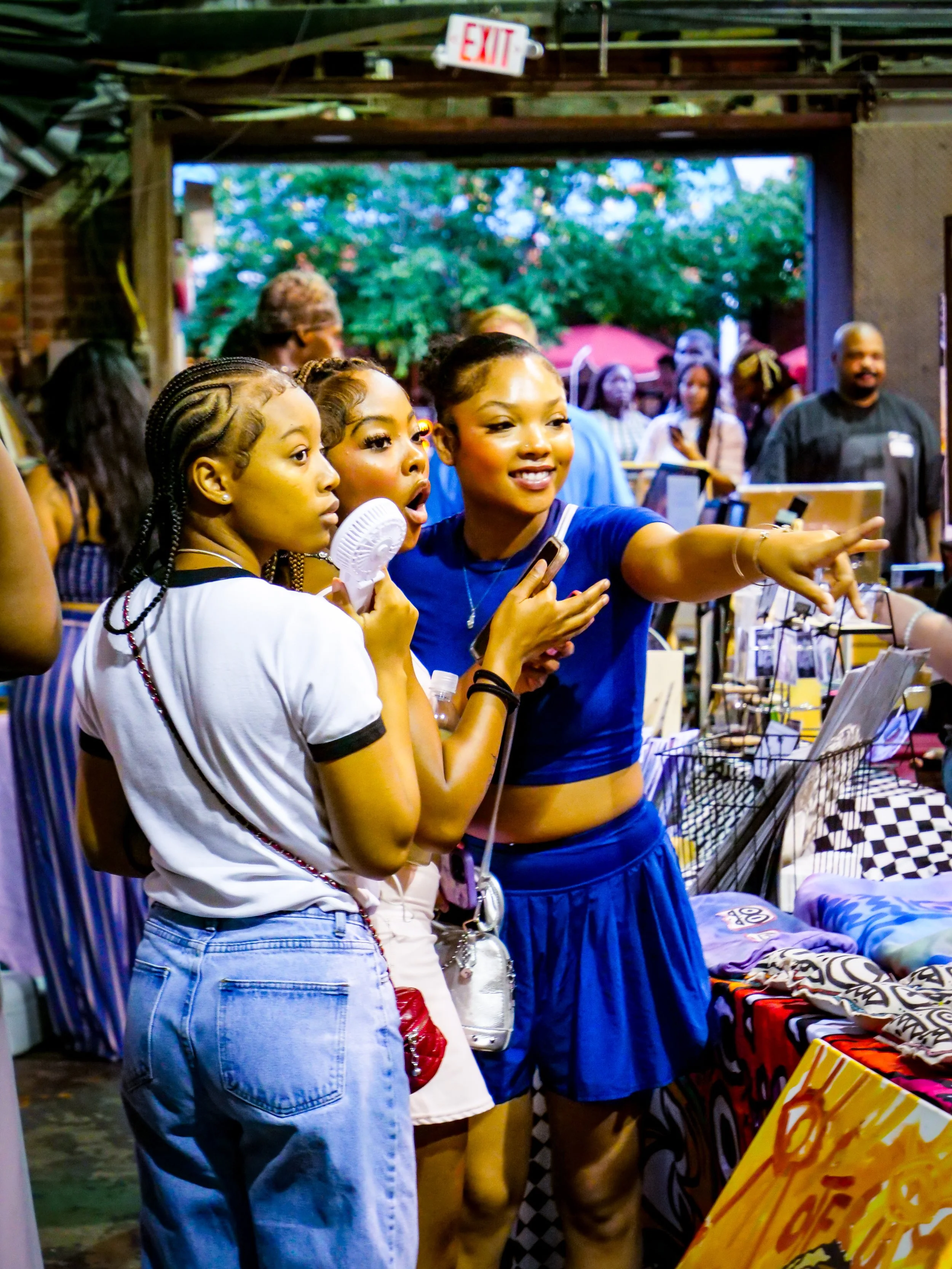 Three women are talking, smiling, and pointing at art 