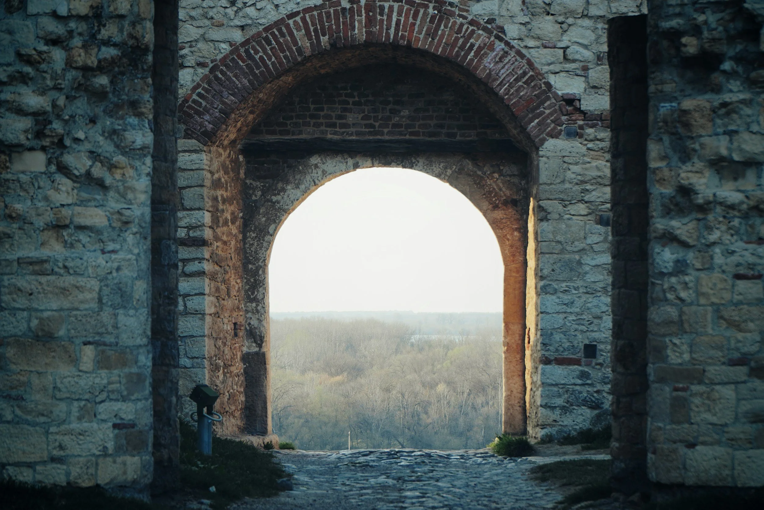 Ancient stone archway with brick accents looking out over a landscape of trees and open land.