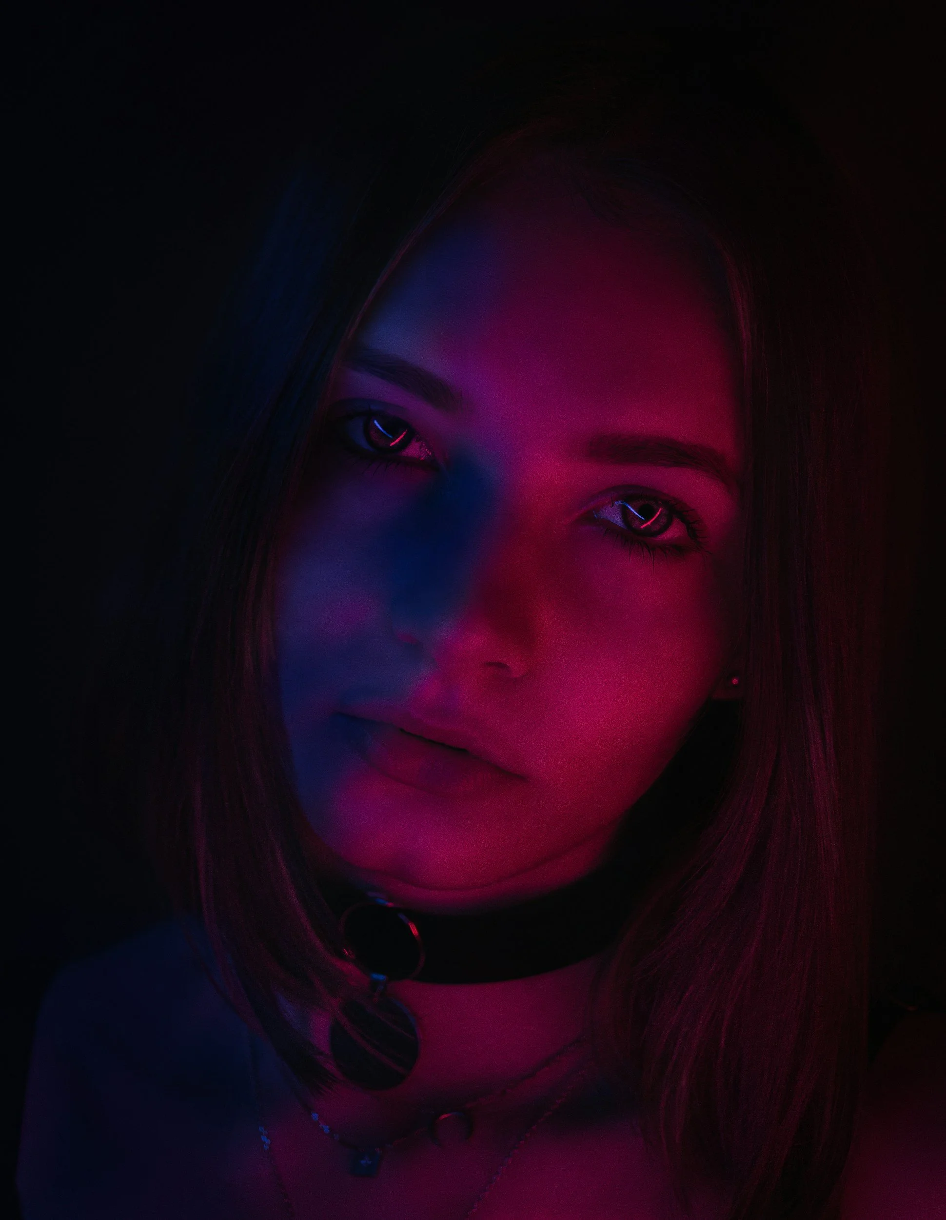 Portrait of a young woman with multicolored neon lighting on her face, dark background.