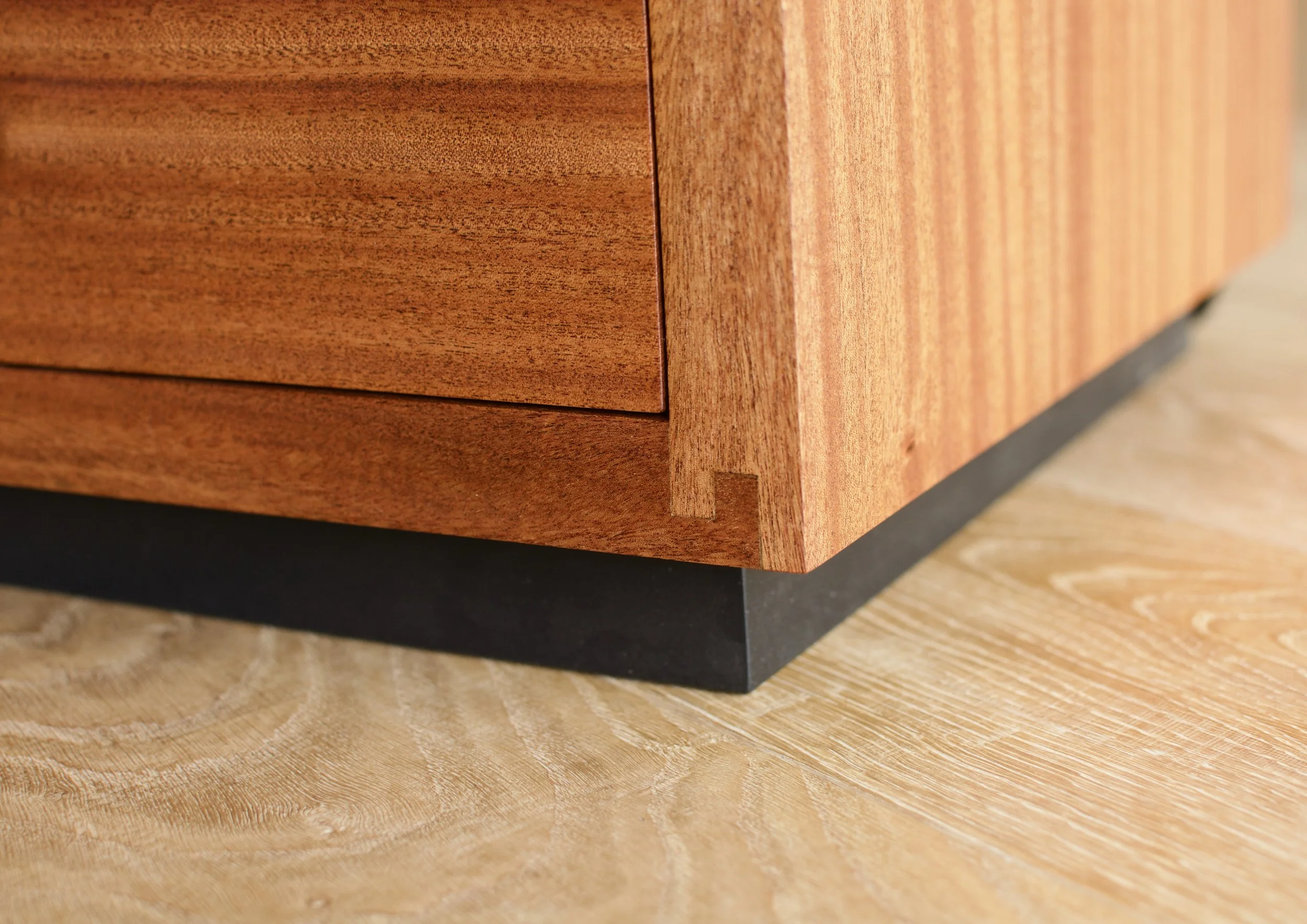 Close-up of a wooden cabinet corner with dovetail joint on a wooden floor.