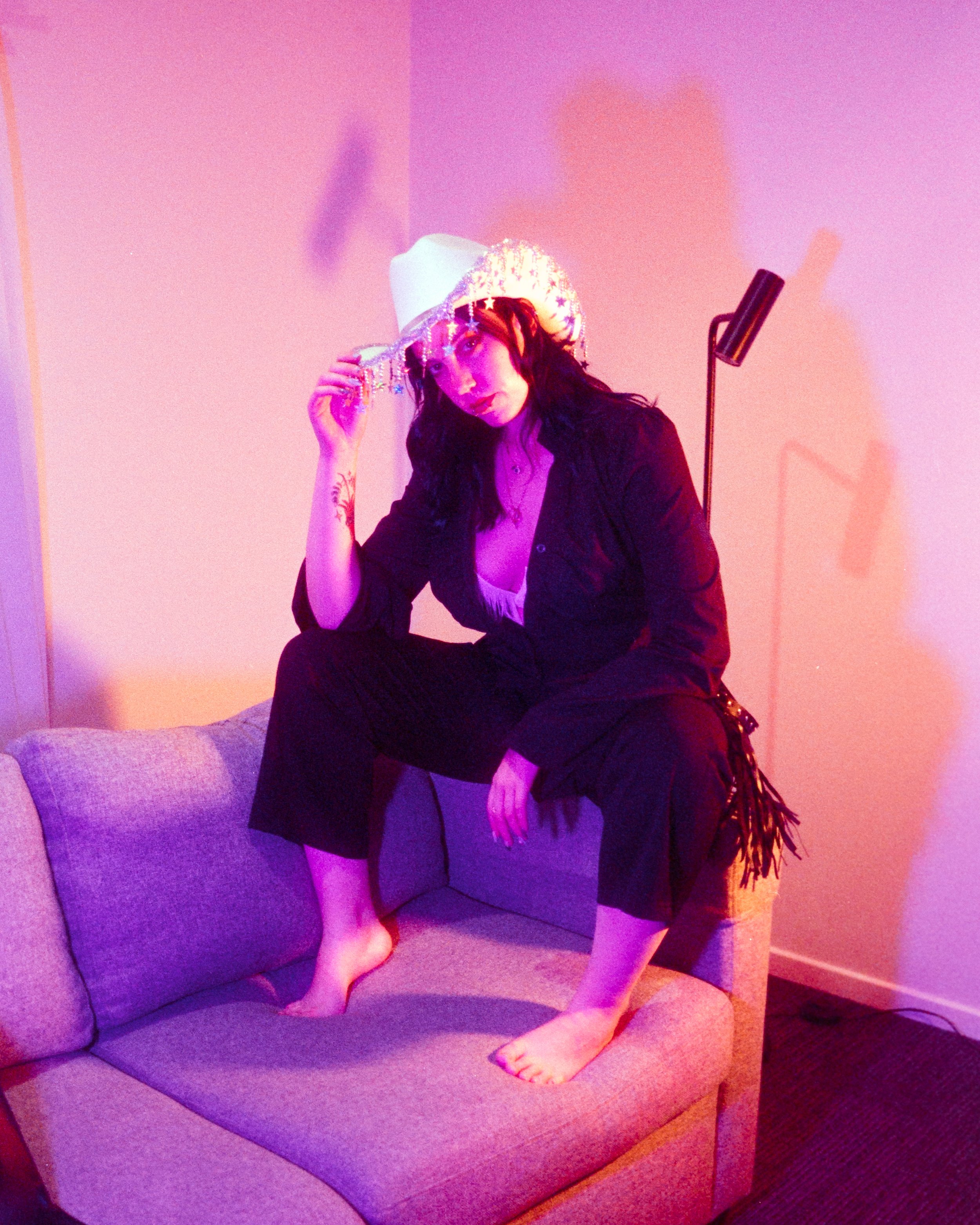 Self portrait of Josie in her Rhinestone Cowgirl outfit, pink and peach lights illuminating her, tilting her hat at the camera, on 35mm Film - 400D Cinefilm
