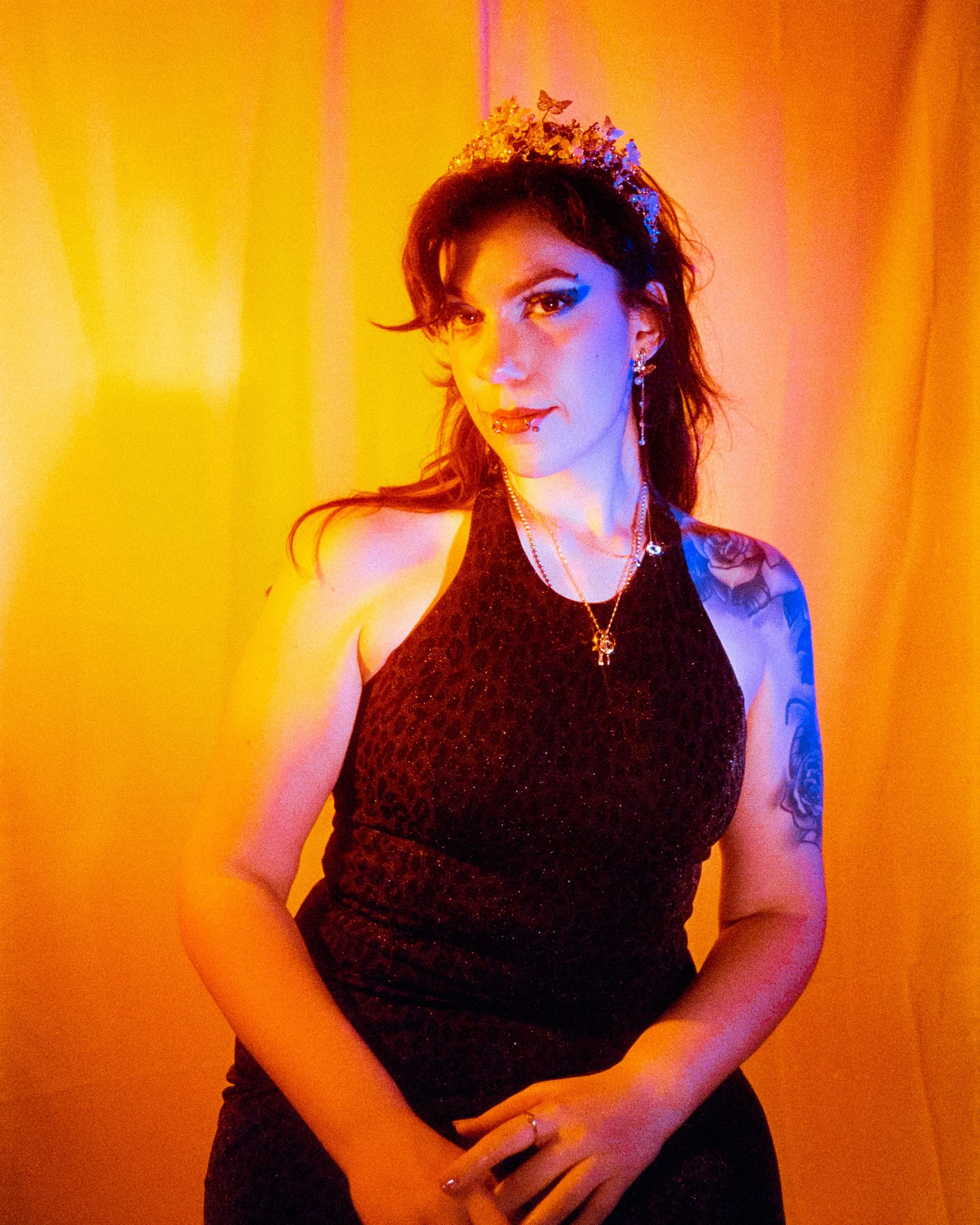 A self portrait of Josie dressed in a leopard print dress, and crown on her head, illuminated by orange and blue lights, on 35mm Film - Ultramax
