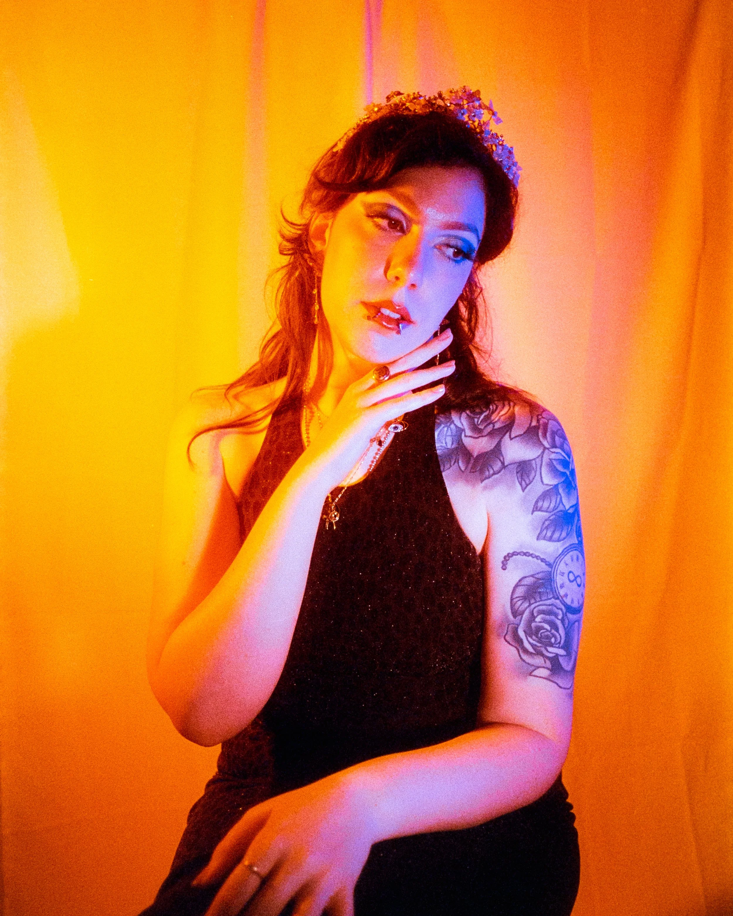 A self portrait of Josie dressed in a leopard print dress, and crown on her head, illuminated by orange and blue lights, her hand under her chin as she looks over her shoulder, on 35mm Film - Ultramax