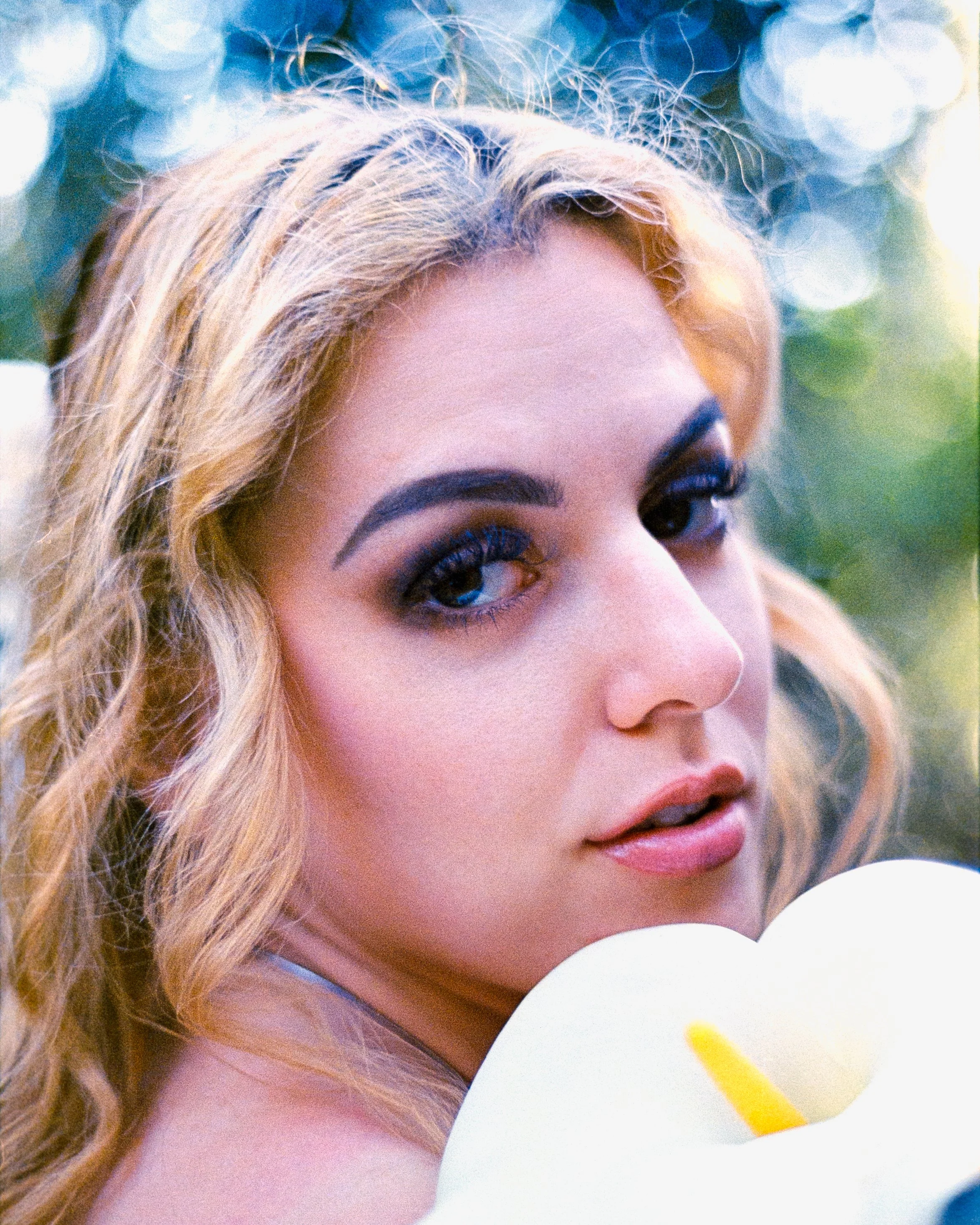 a close up portrait of a woman, her glossy pink lips, her holding a flower to her face, looking directly at the camera softly, on 35mm Film - Ultramax