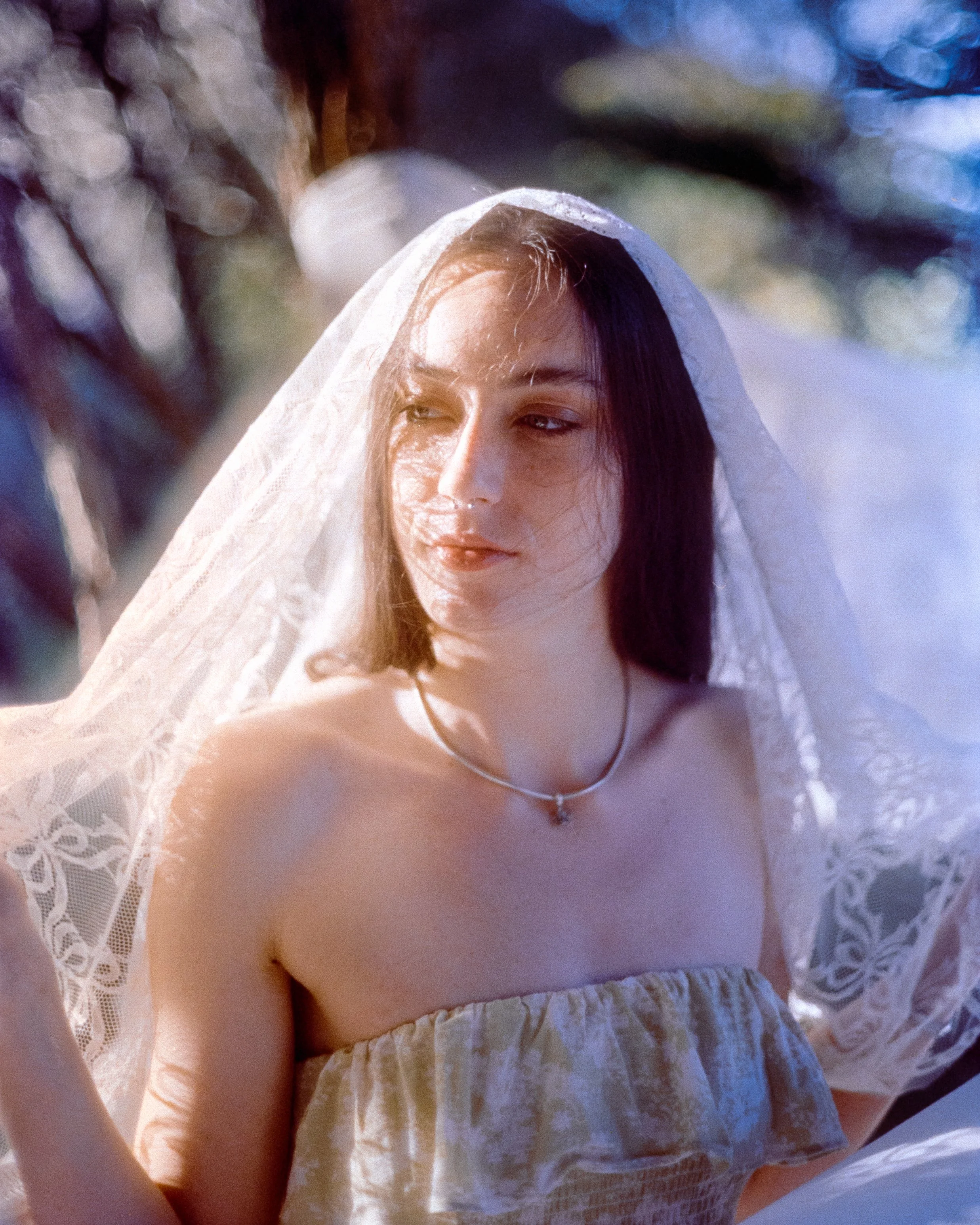 a woman with a lace veil over her head, golden sunlight casting soft shadows and shapes on her face as she looks off over her shoulder slightly, on 35mm Film - 200T Cinefilm