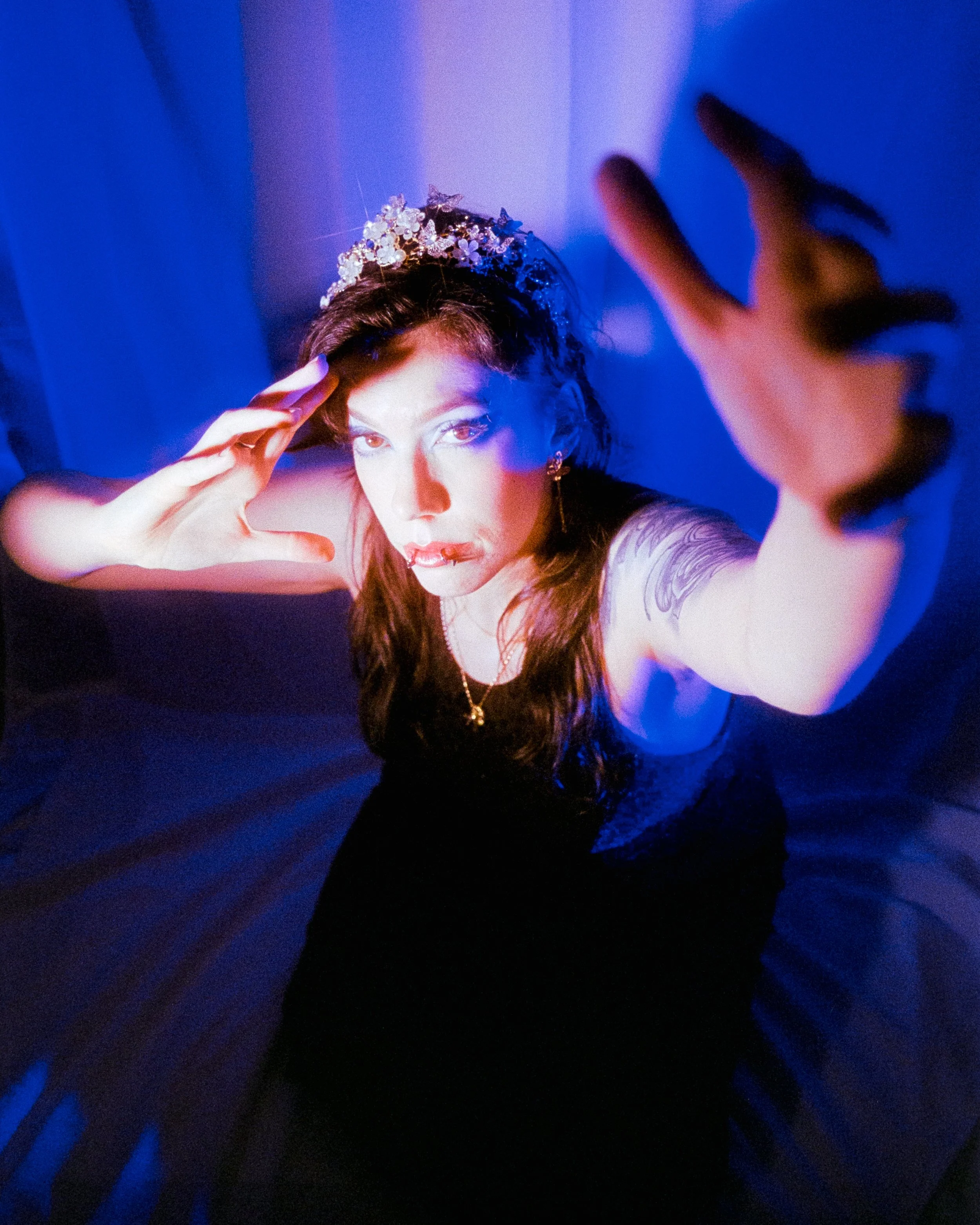 A self portrait of Josie dressed in a leopard print dress, and crown on her head, illuminated by white and blue lights and she dramatically reaches towards the camera, on 35mm Film - Ultramax