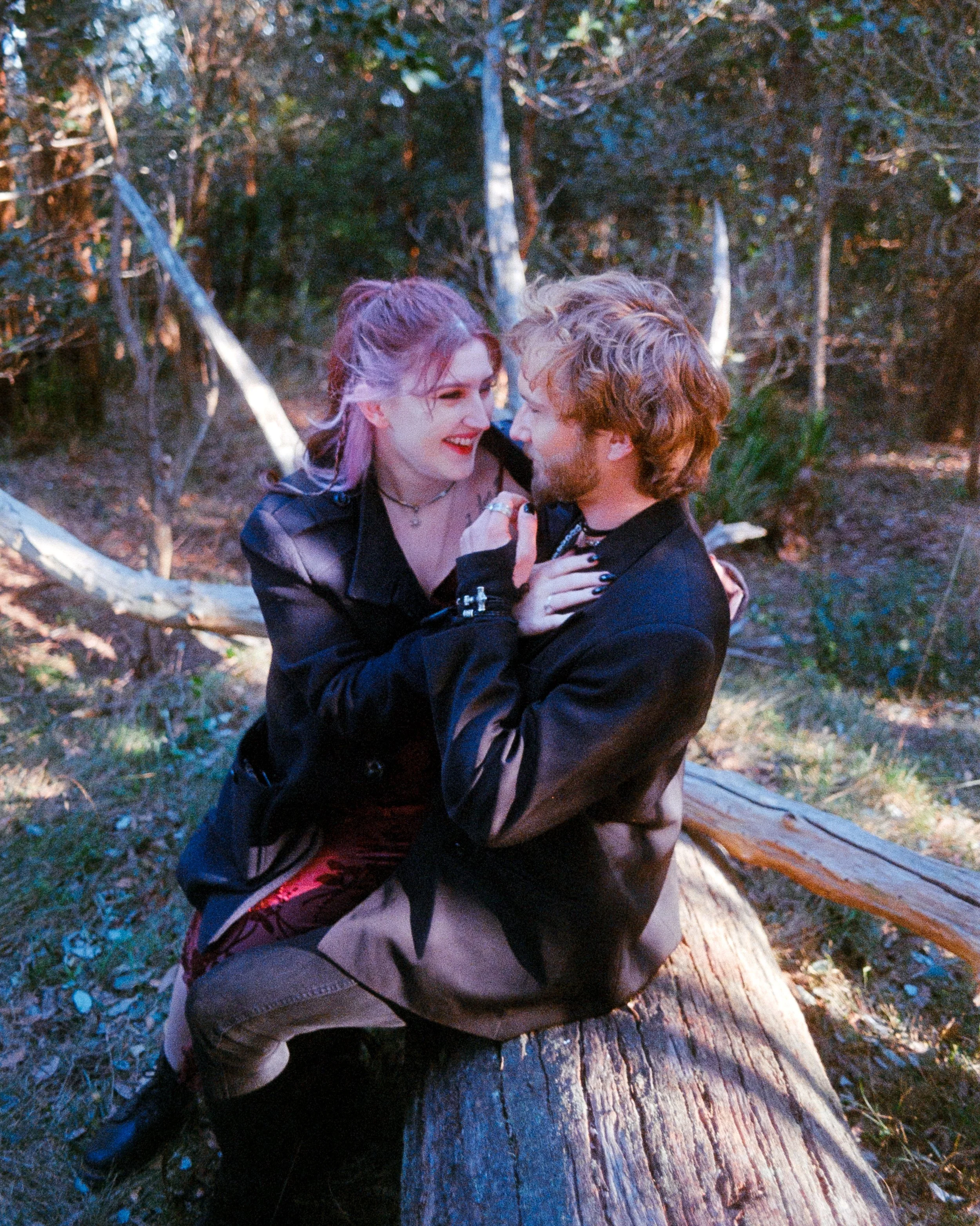 a couple holding one another and laughing while sitting on a large log in the forest, illuminated by golden sunlight, captured on 35mm Film - Ultramax