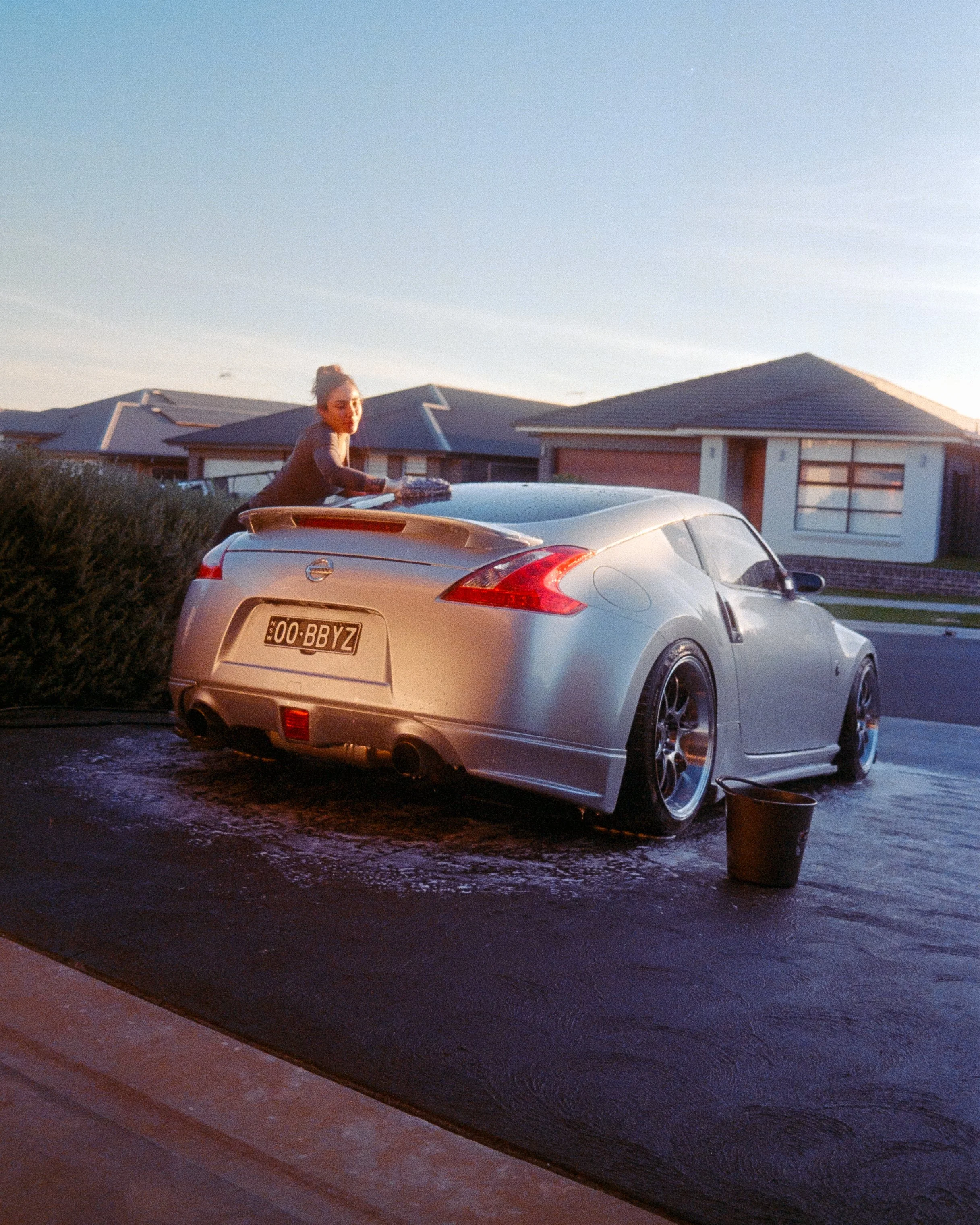 Rear shot of a Nissan 270z and the owner Nicole washing her car, the silver of the car glowing in the sun, shot on 35mm Film - Kodak Gold