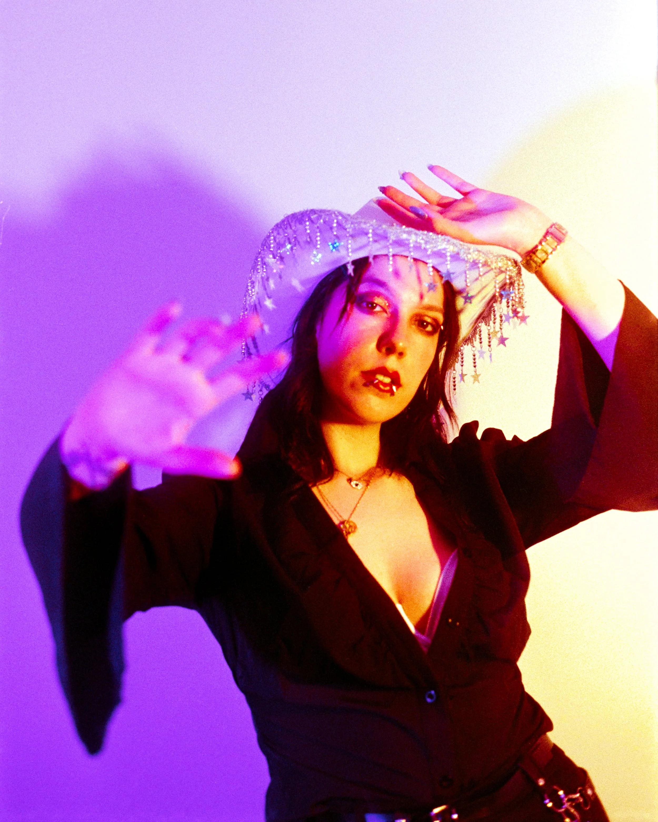 Self portrait of Josie in her Rhinestone Cowgirl outfit, pink and peach lights illuminating her, reaching one hand towards the camera, the other over her head, on 35mm Film - Ultramax