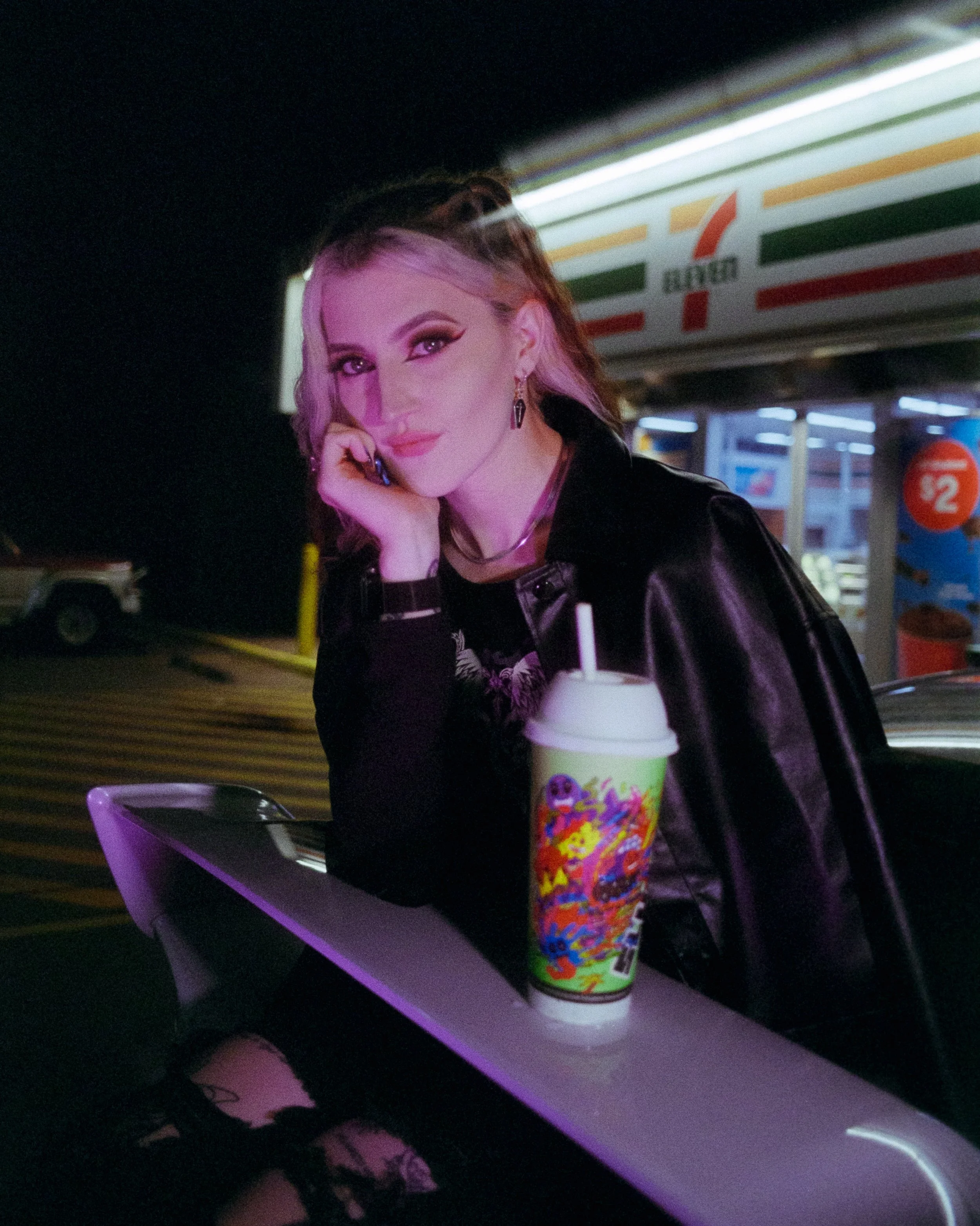 A portrait of Melody, the owner of a Subaru WRX, sitting under the wing of her car at 7Eleven, with a slurpee, illuminated by purple light, shot on 35mm Film - Ultramax pushed to 800