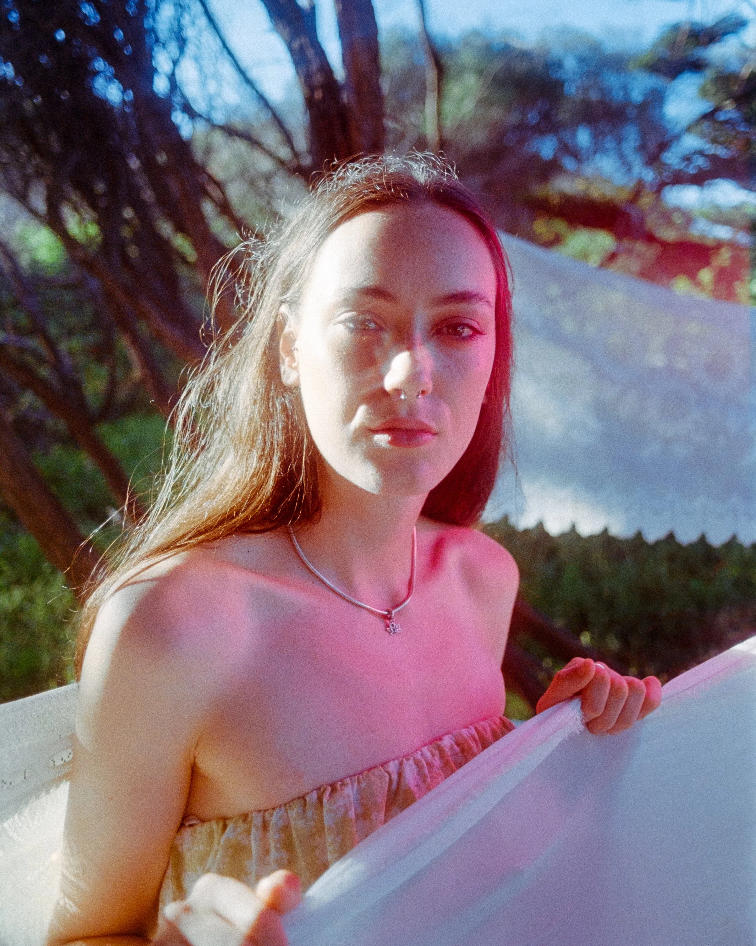 A glowing portrait with golden sunlight, starbursts, and pink lighting, while the woman looks softly at the camera creating a romantic image, on 35mm Film - Ultramax