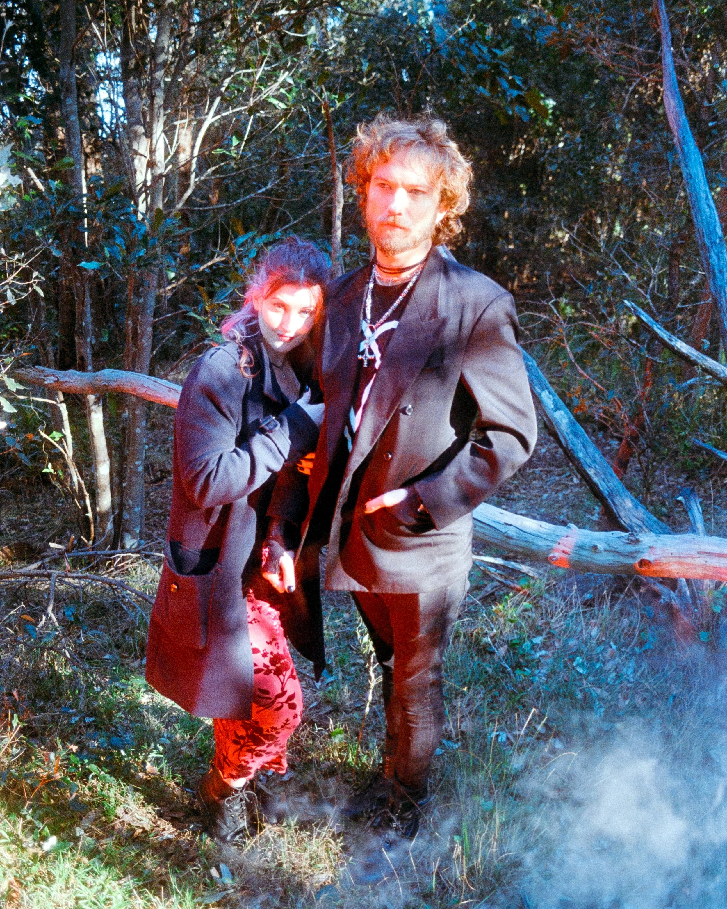 Alternative couple in the forest, smoke around them, both in red and black, holding one another, captured on 35mm Film - Ultramax
