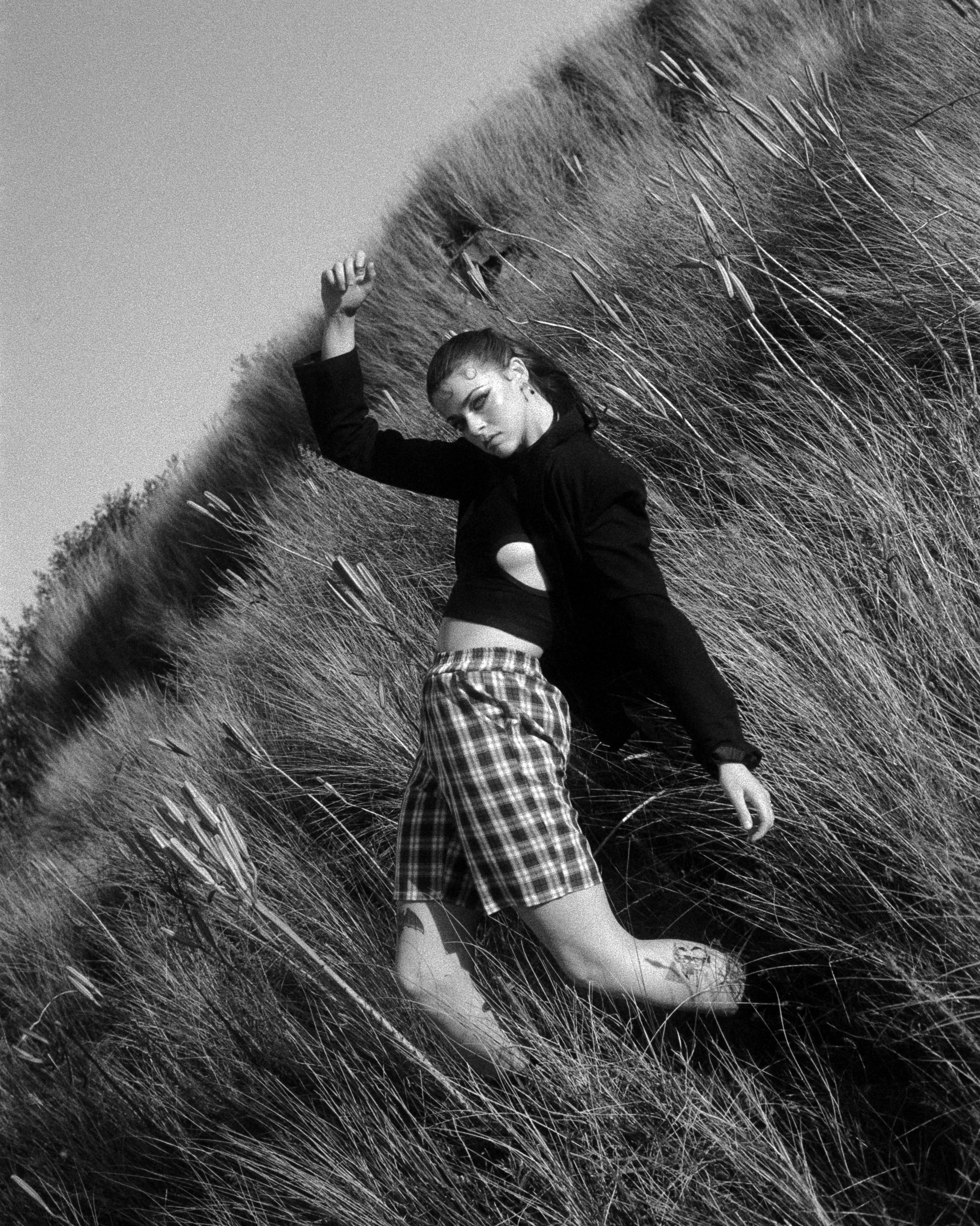 a dynamic shot of Elle Farrow in the tall grass at Bombo, dressed in a suit, leaning back dramatically, on 35mm Film - Fomapan 400