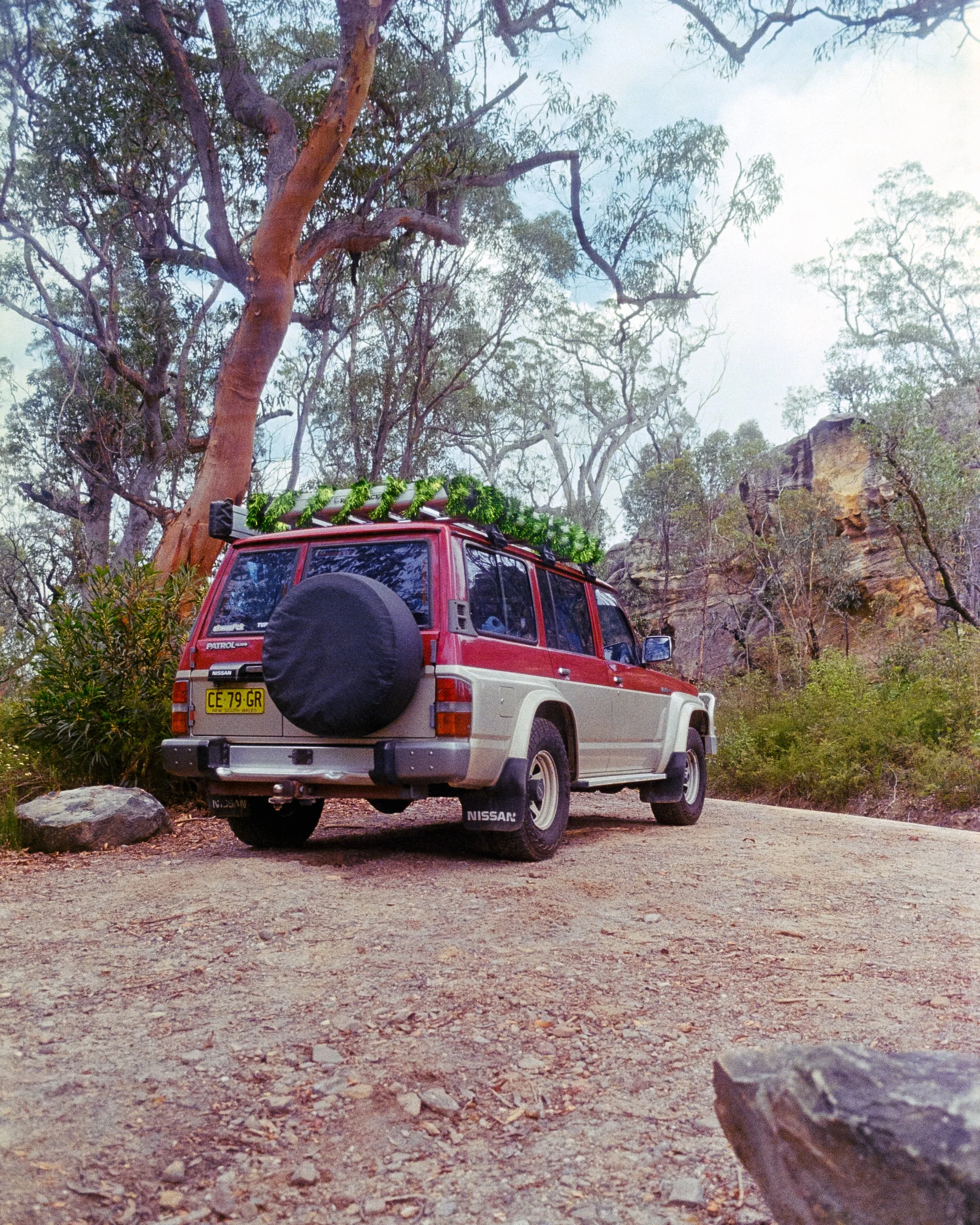 A rear 3/4 shot of Scorpion, Josie's GQ Patrol, with tinsel wrapped around the roof rack, out in the forest, shot on 35mm Film - Ultramax