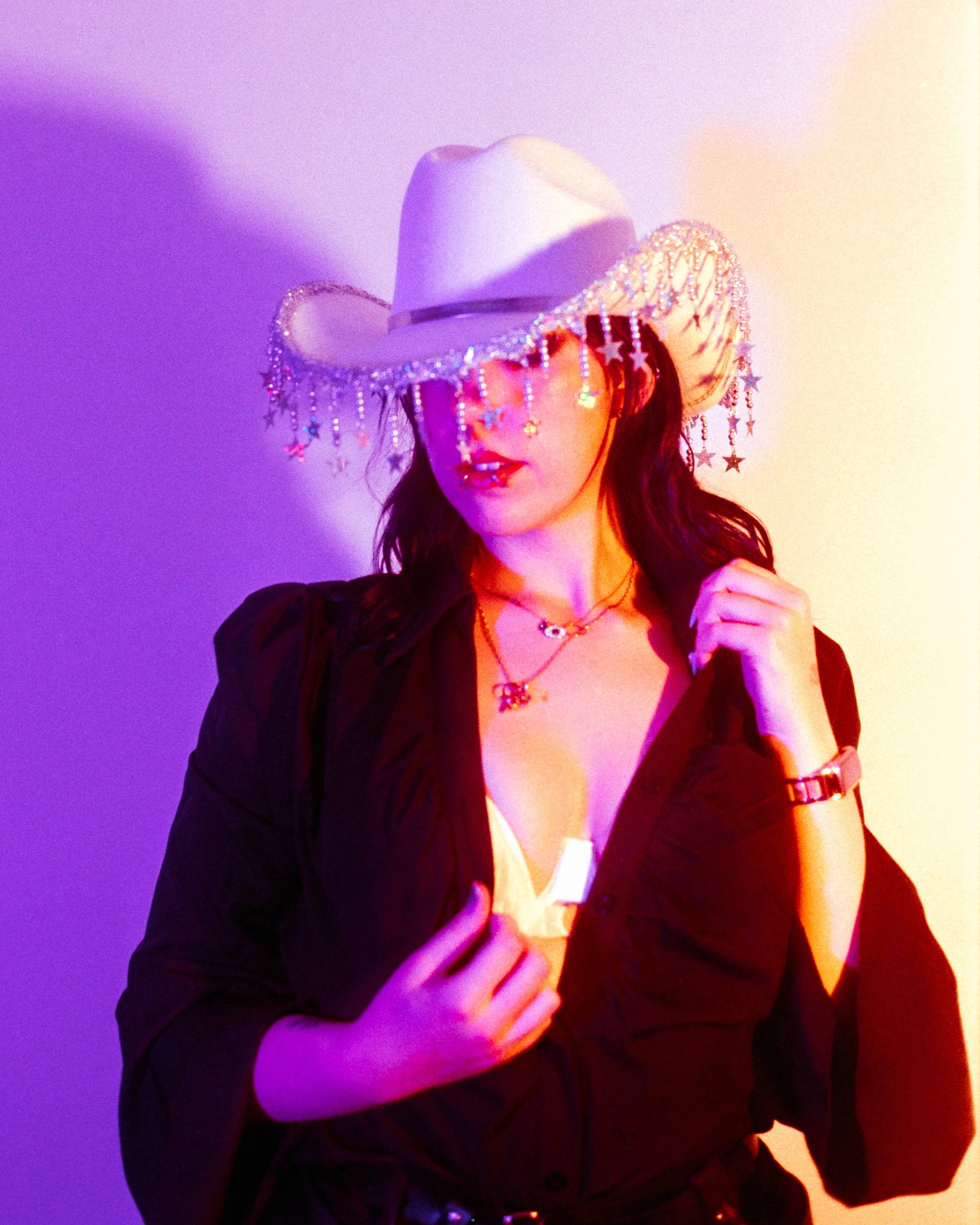 Self portrait of Josie in her Rhinestone Cowgirl outfit, pink and peach lights illuminating her, her face partially hidden by her hat, on 35mmFilm - Ultramax
