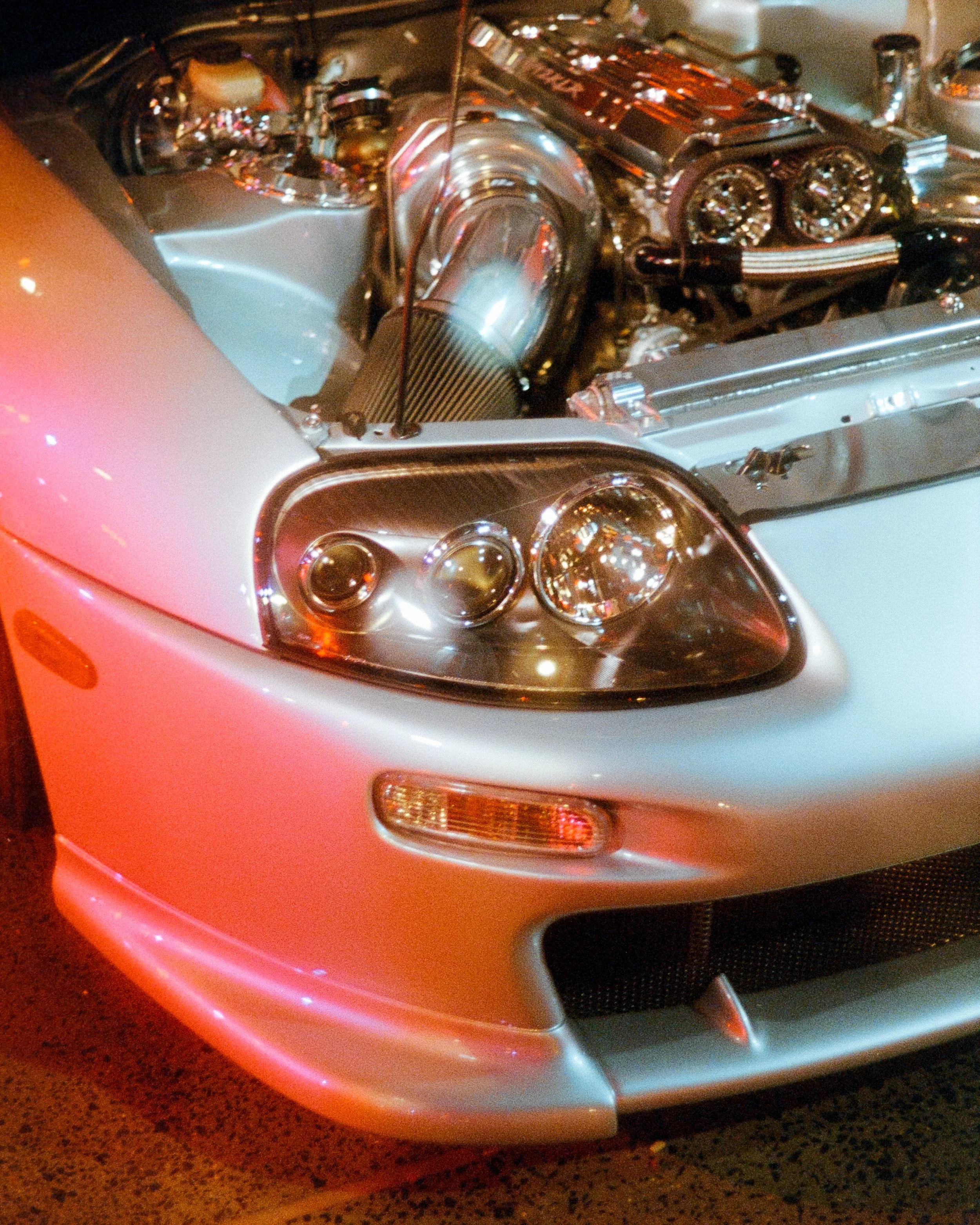 Glowing headlight shot of a Supra, lit up by red spotlights, shot on 35mm Film - Ultramax