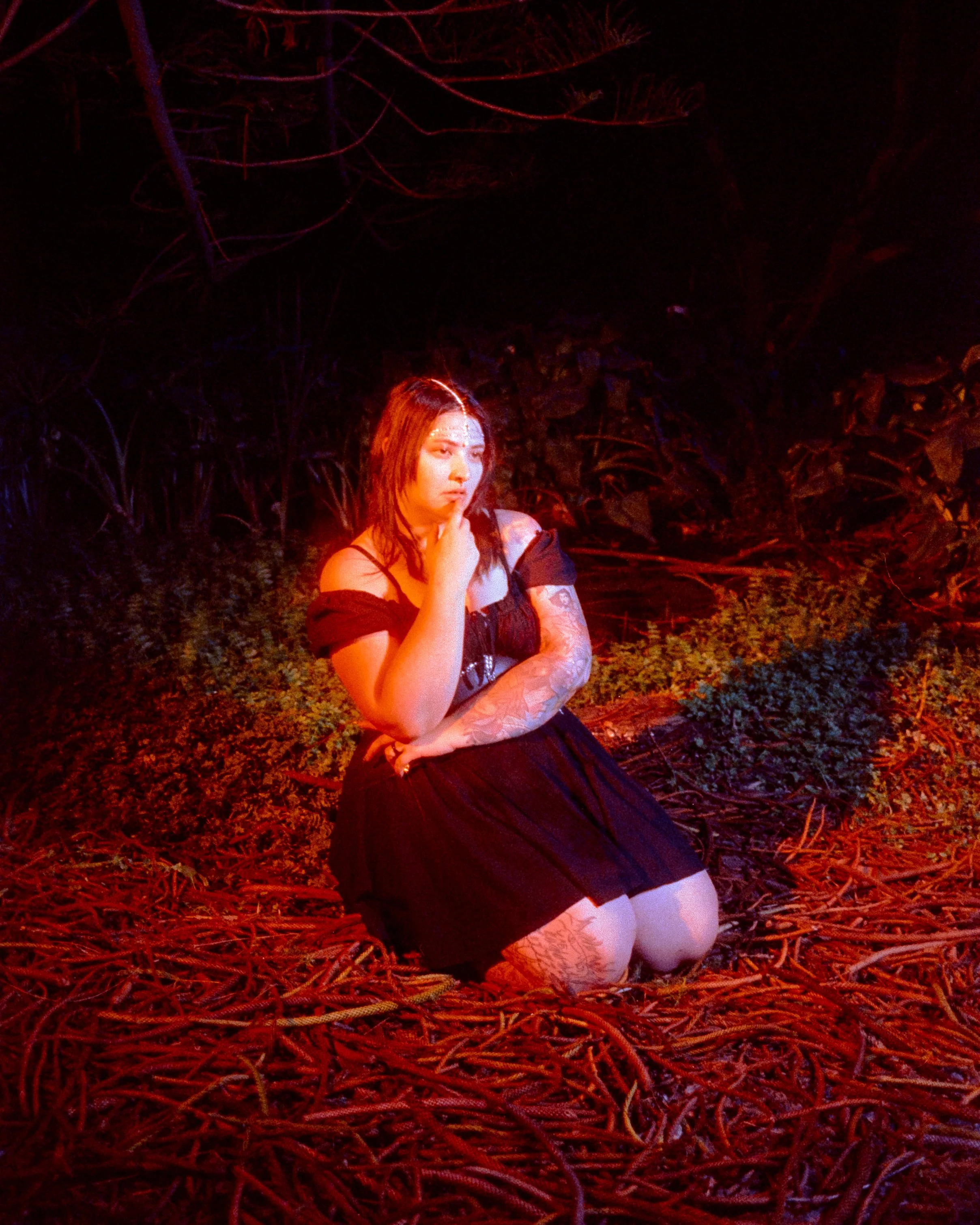 A portrait of Gabby, kneeling in the forest, hand on her chin, looking off into the distance, shot on 35mm Film - 500T Cinefilm