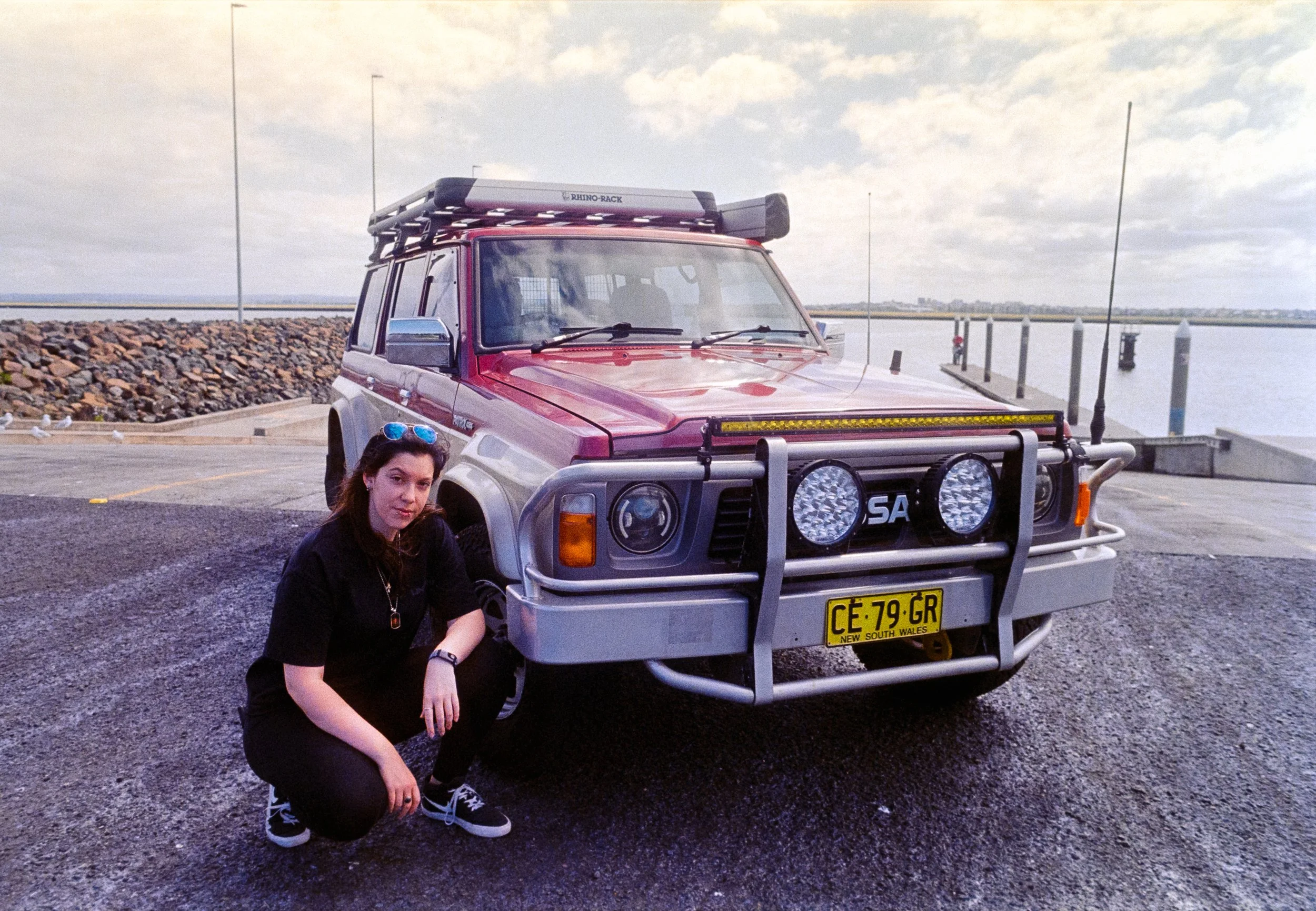 Josie crouched down next to Scorpion, her GQ Patrol, out at Port Botany Boat Ramp, on 35mm Film - Ultramax