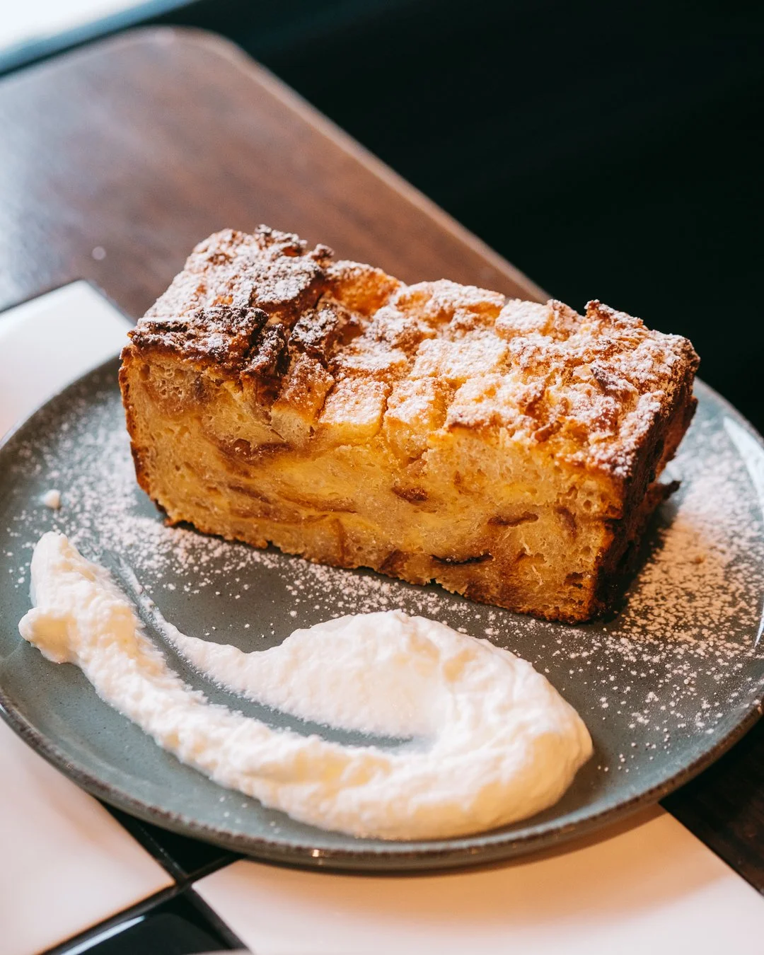 Slice of apple cake dusted with powdered sugar on a gray plate, served with a dollop of whipped cream.