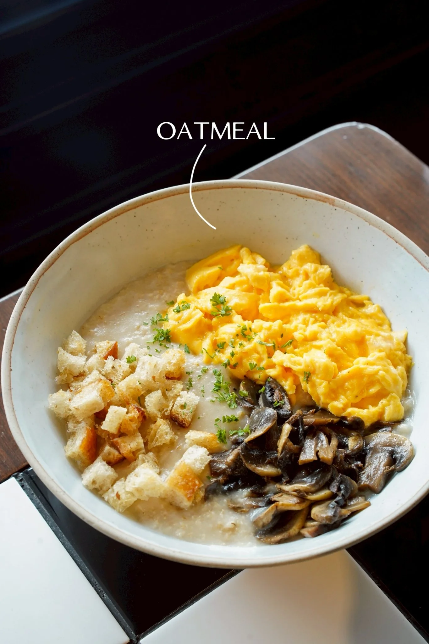 Bowl of oatmeal with scrambled eggs, sautéed mushrooms, and croutons, garnished with parsley.