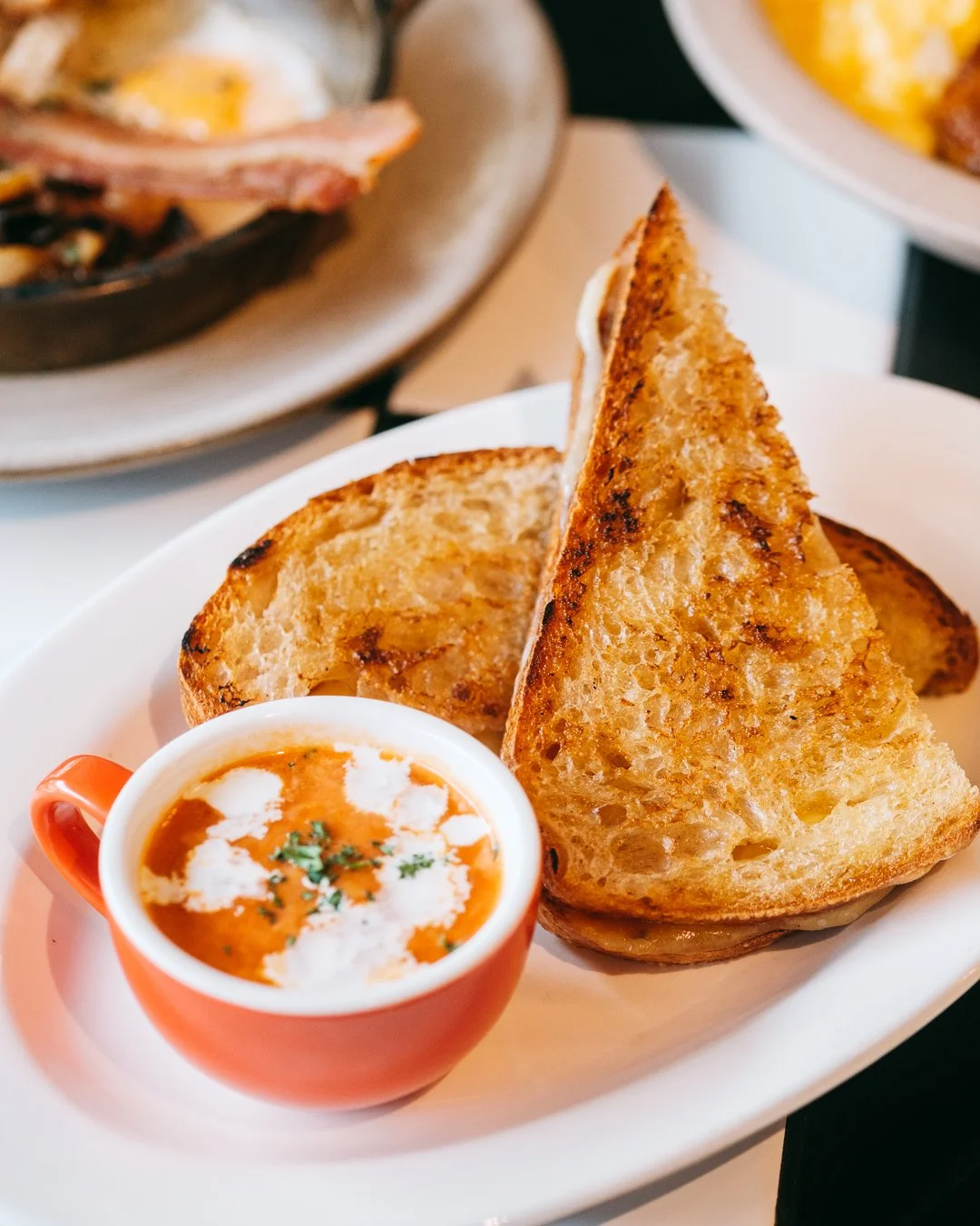 Close-up of grilled bread slices served with a small cup of tomato soup garnished with cream and herbs.