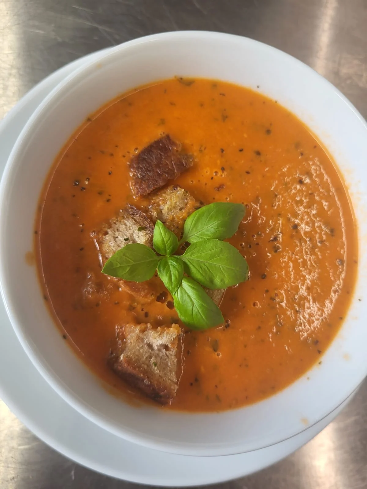 Tomatensuppe mit Basilikumblättern und Croutons in einer weißen Schüssel