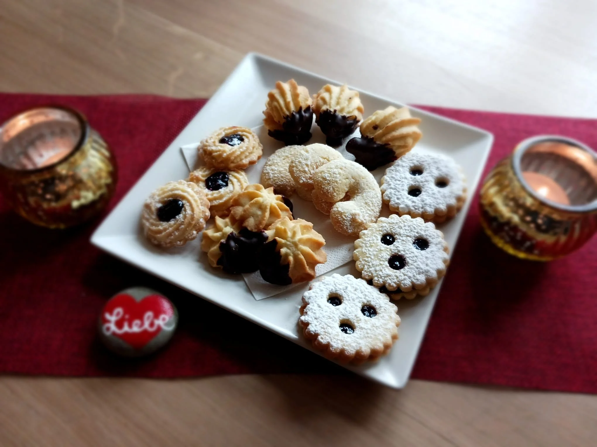 Bunte Kekse und Süßigkeiten auf einem weißen Teller, umgeben von Weihnachtsartikeln.