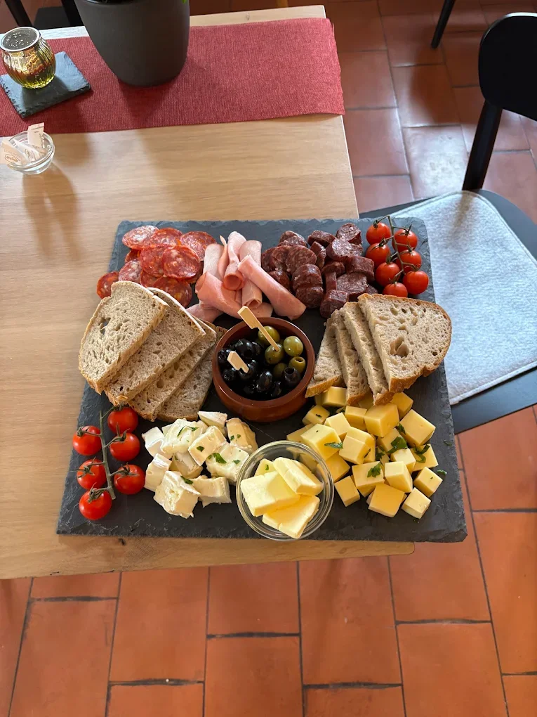 Käseplatte mit Tomaten, Wurst, Salami, Brot, grünen und schwarzen Oliven, Kirschtomaten, und weitere Käsewürfel, alles auf einem schwarzen Steinplattenteller.