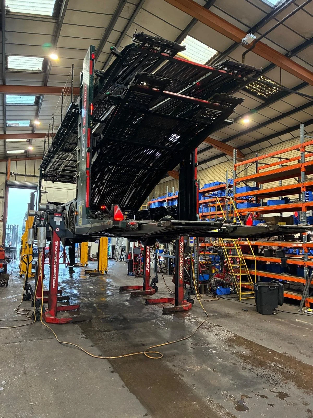 A car lift inside a warehouse with shelves and tools, with a car on the lift being serviced.