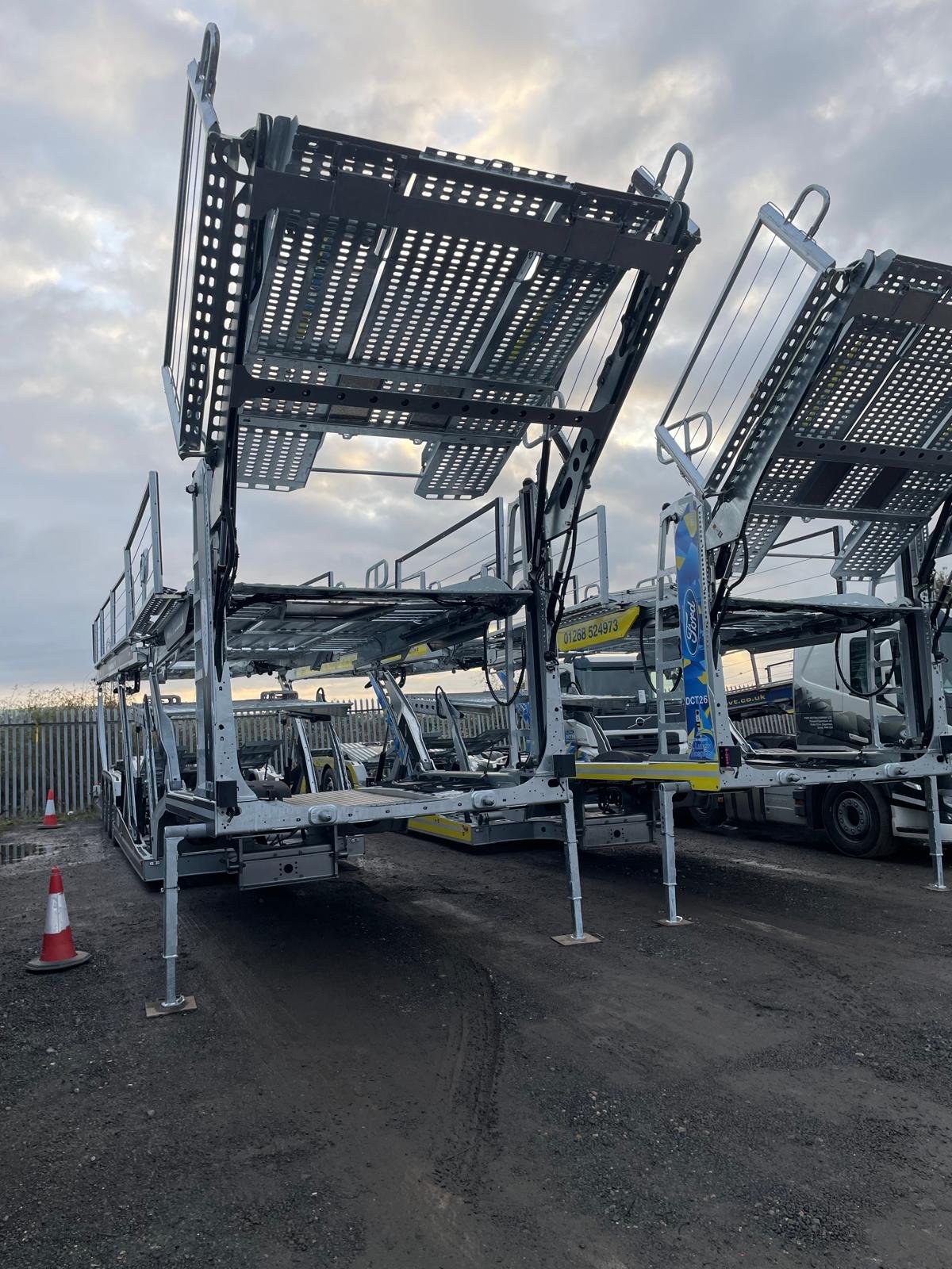 Two large empty car carrier trailers parked outdoors on a dirt lot with cloudy sky above.