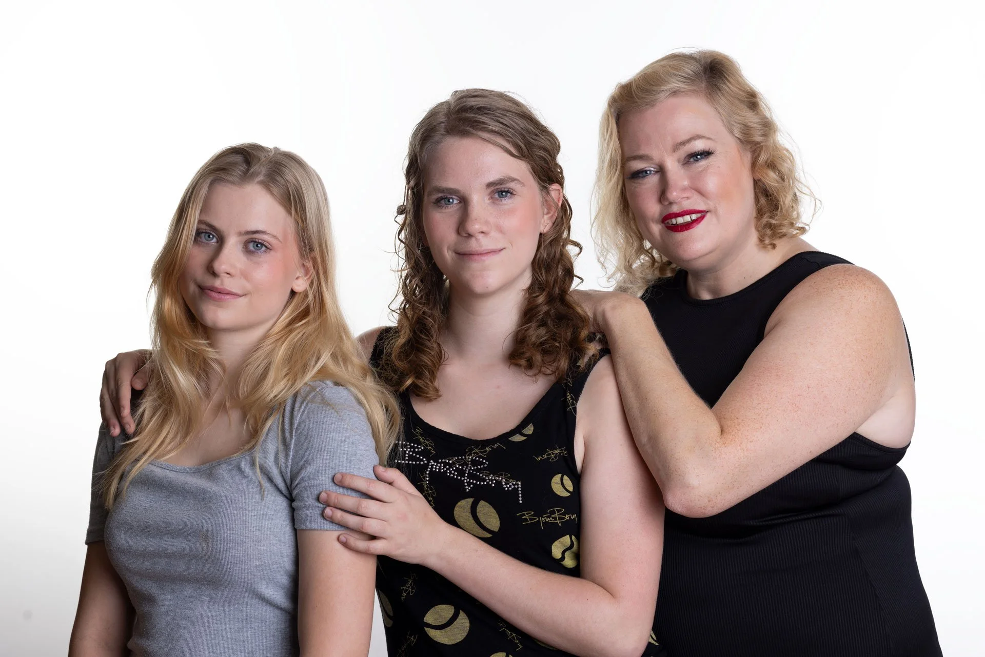 Tre kvinder står tæt sammen mod en hvid baggrund, smiler og ser i kameraet.