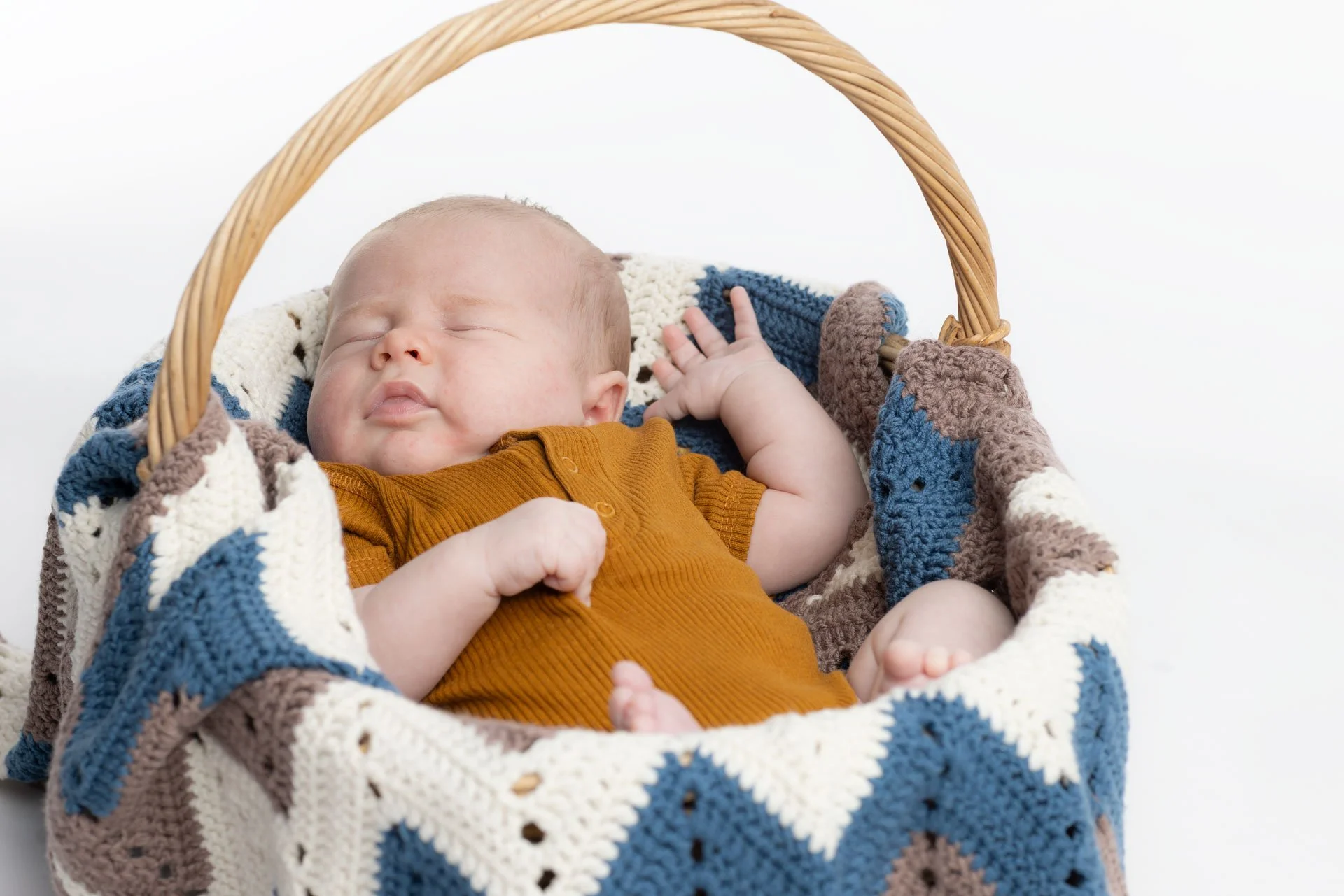 Søvnende baby i en kurv med et farvet strikket tæppe.