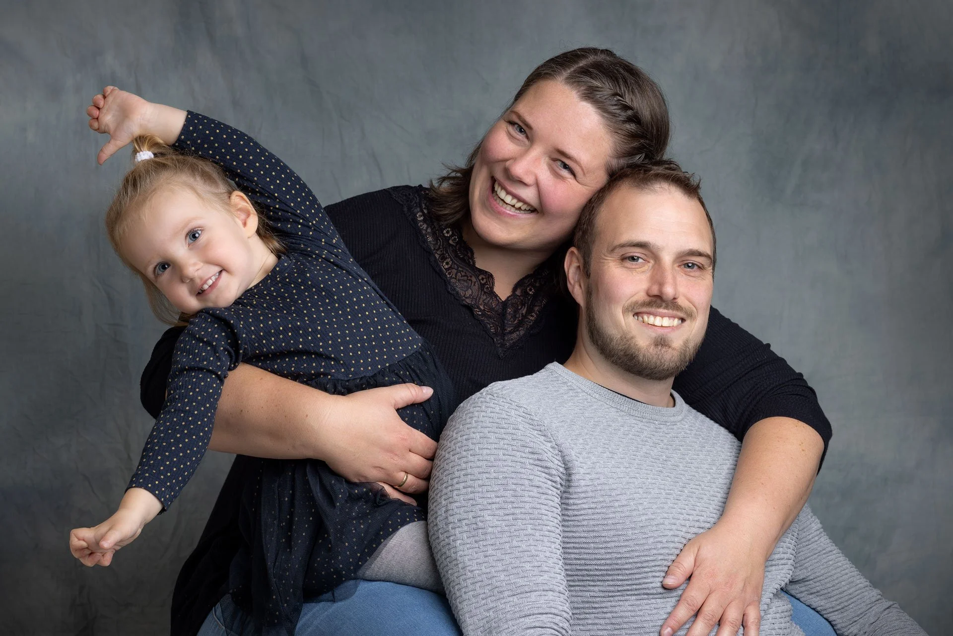 Et smilende familie portræt med tre personer: En ung pige, en kvinde og en mand, der alle nyder hinanden.
