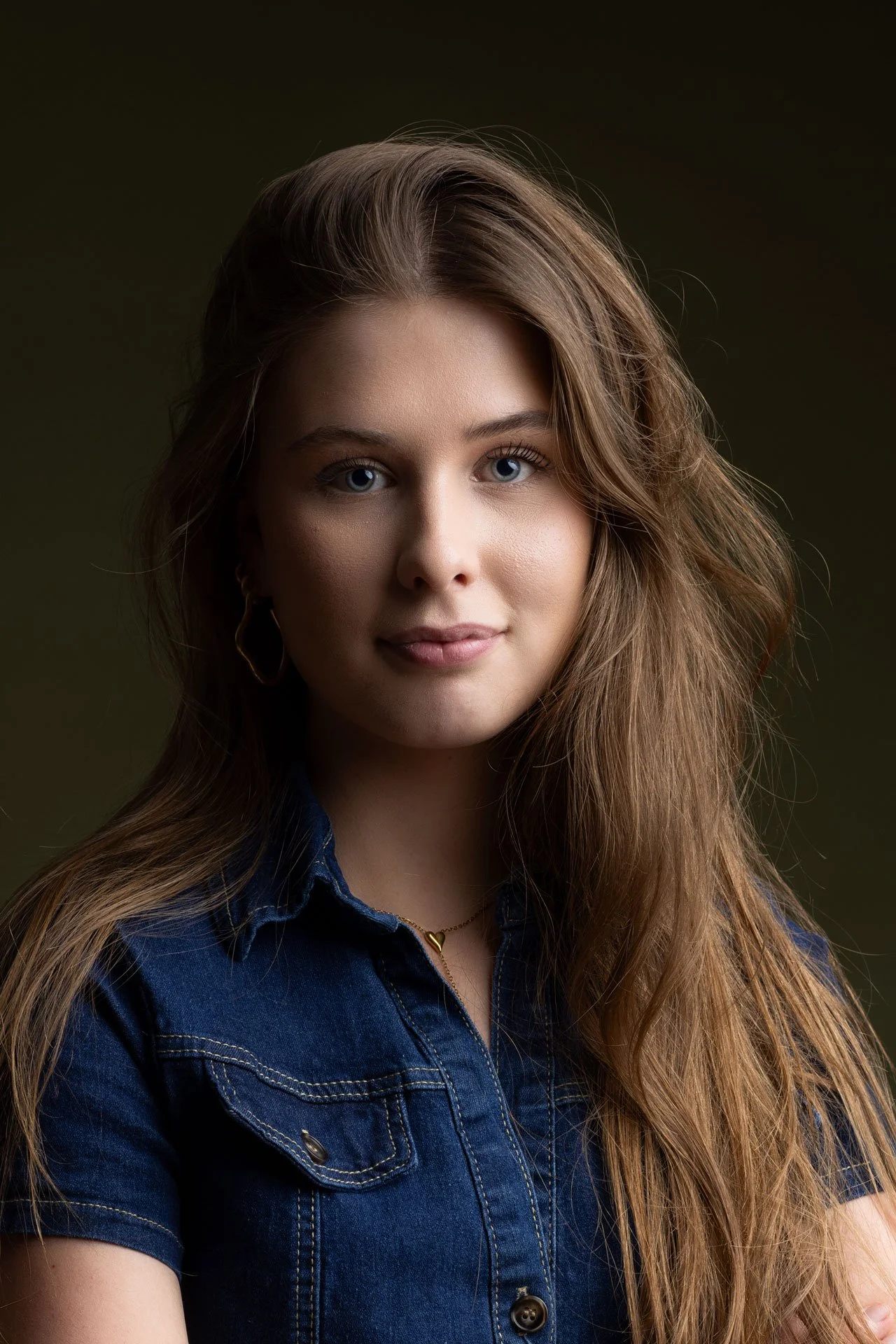 Portræt af en ung kvinde med langt, lyst hår iført en denim skjorte og halskæde med hjerteformet vedhæng.