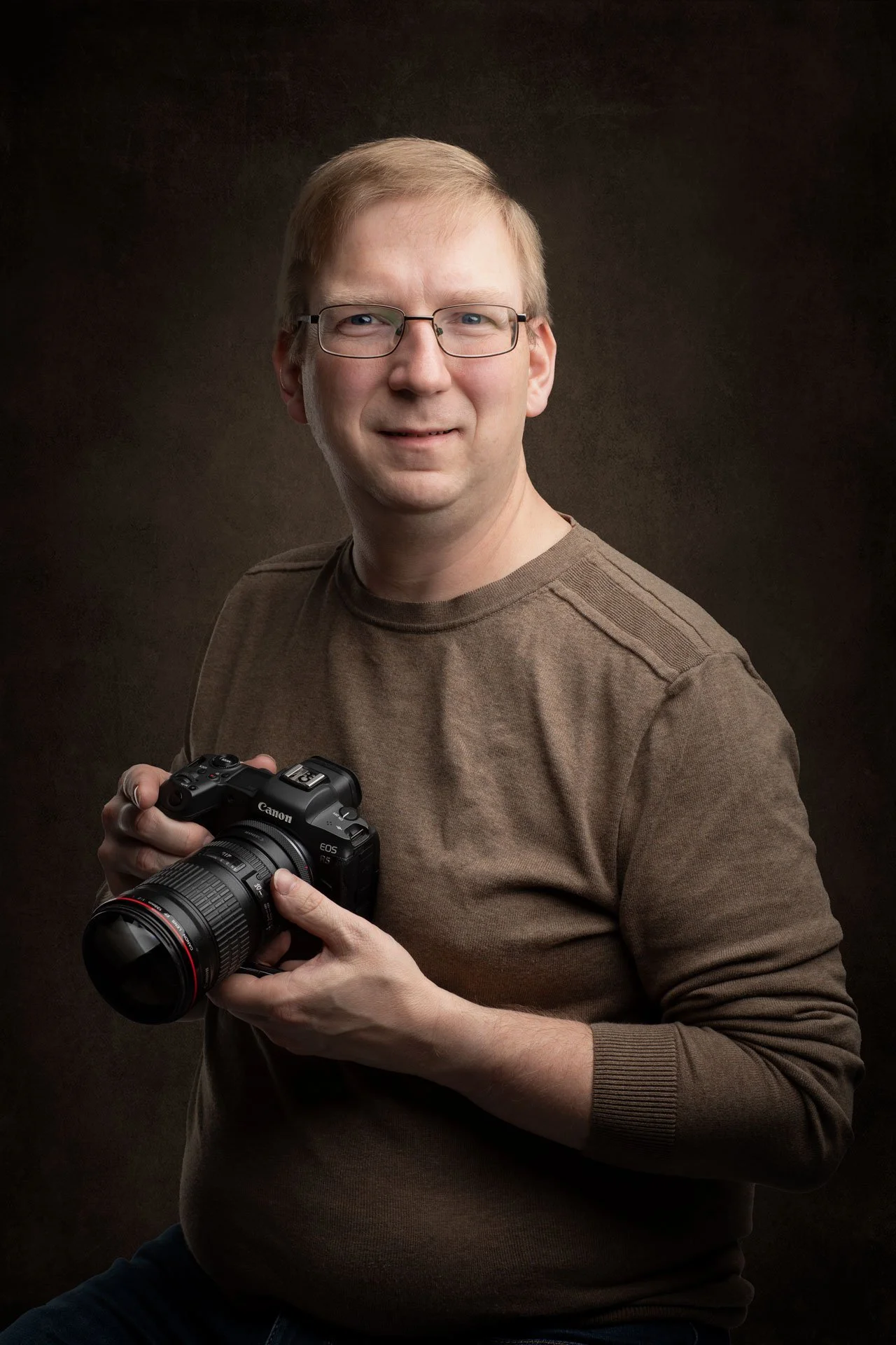 En mand med brunt sweater og briller holder et Canon kamera.