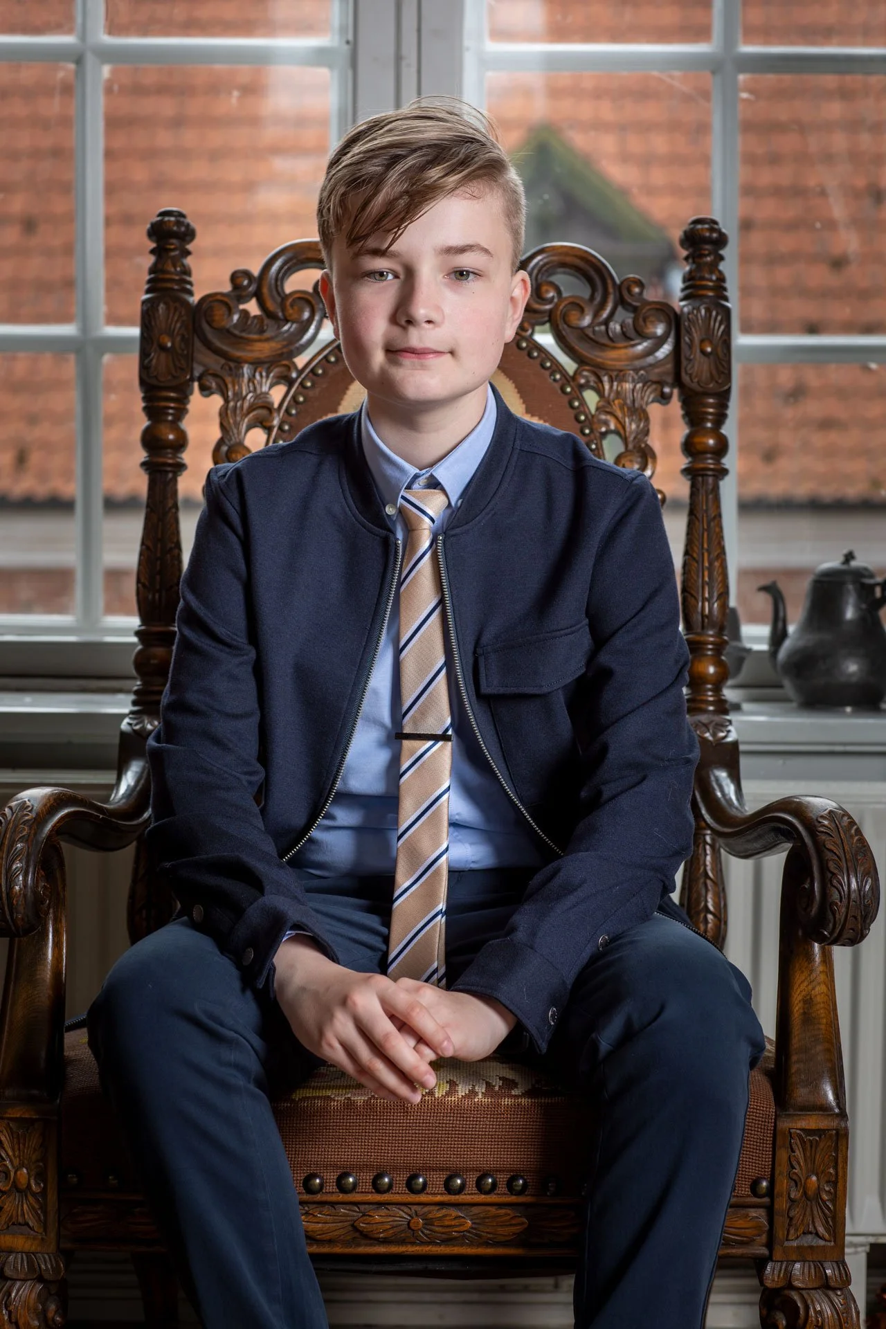 En dreng sidder i en træstol foran et vindue.