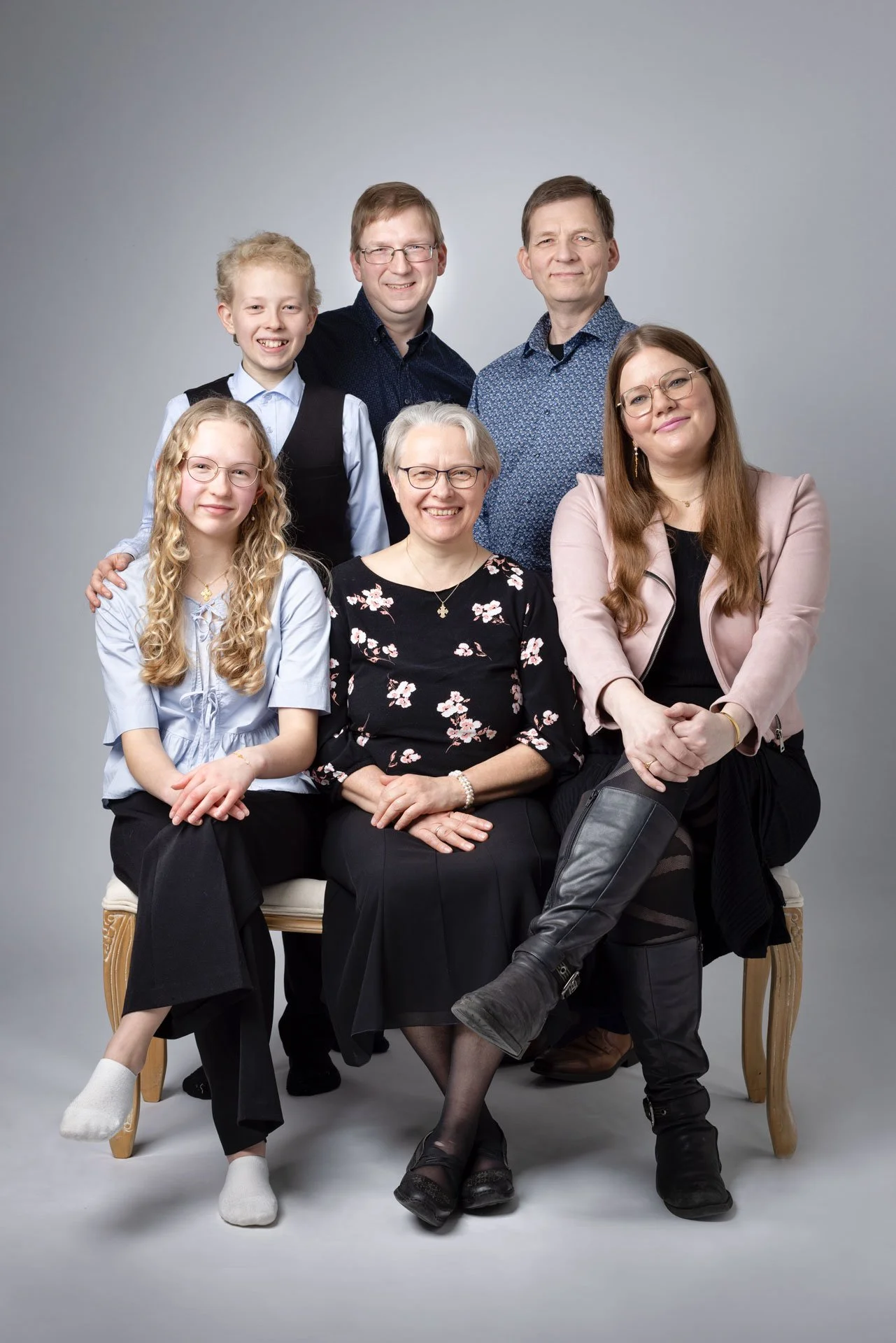 Familiegruppe portræt med ni personer, siddende og stående mod en neutral grå baggrund, alle smilende, forskellige aldre, kvinder, mænd og børn.