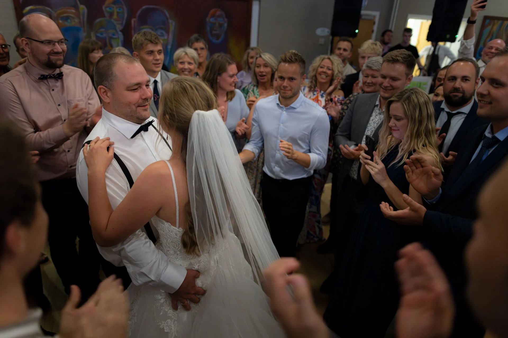 Bryllupsscene med brudepar og gæster, der danser i en festlig atmosfære.